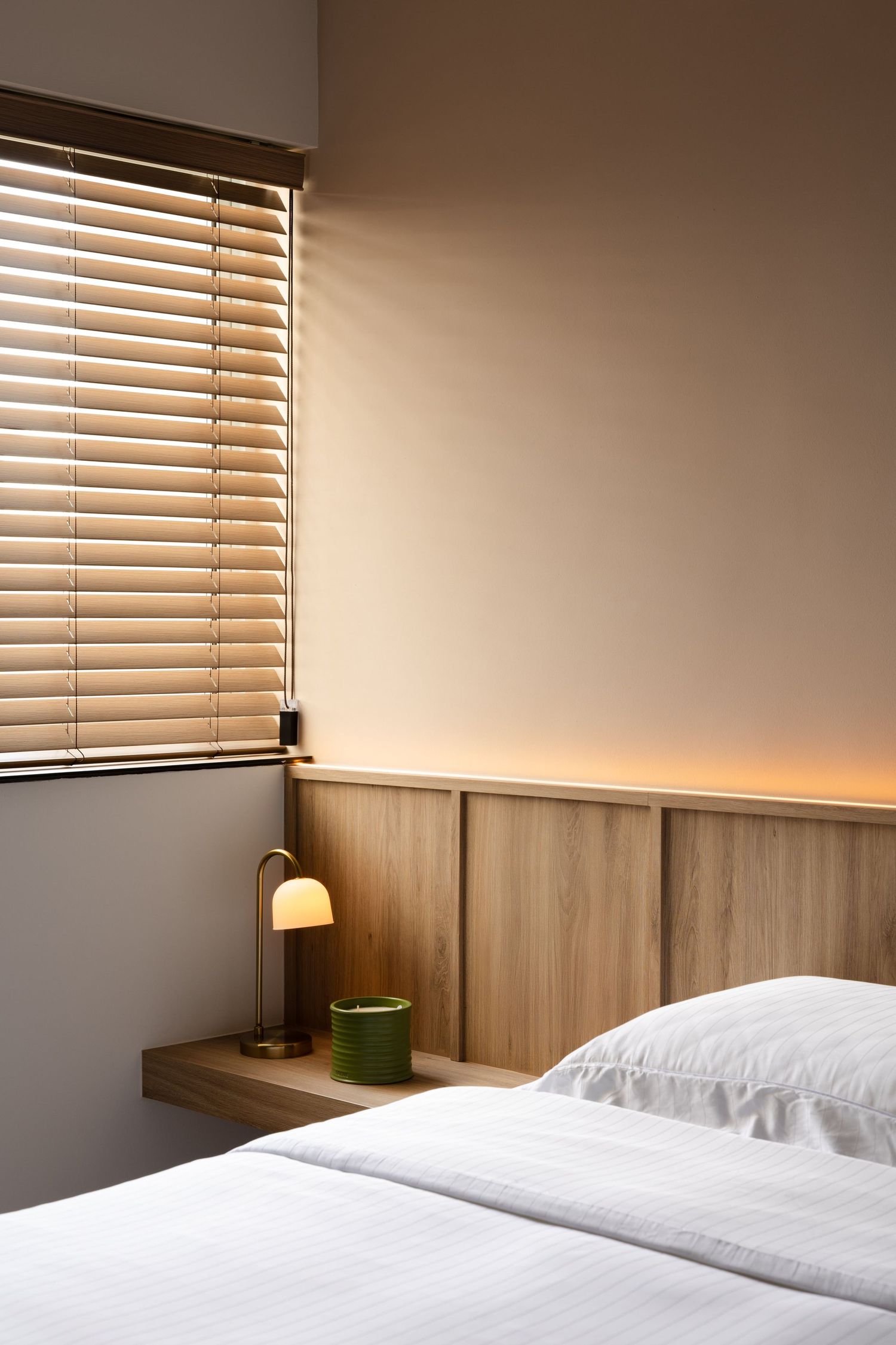 Minimalist bedroom interior with wooden wall panels and venetian blinds creating warm ambient lighting.