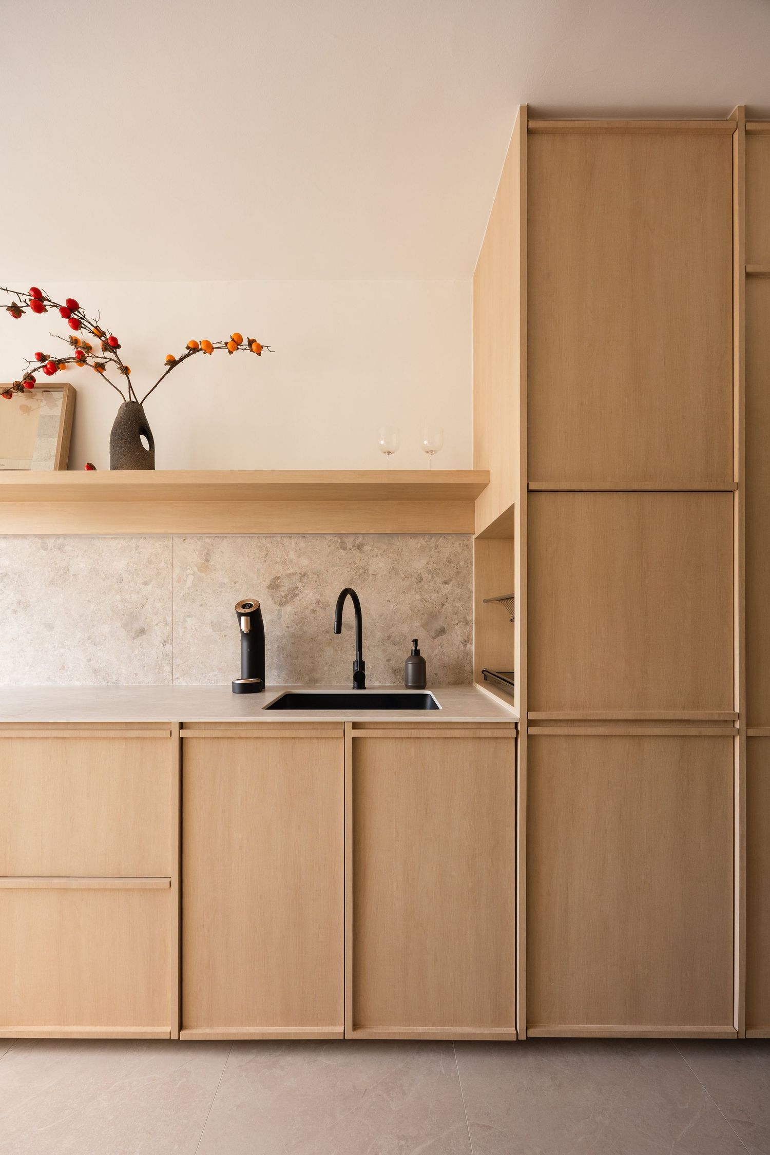 Modern minimalist kitchen interior with light wood cabinets and white walls features sleek black hardware and fixtures.