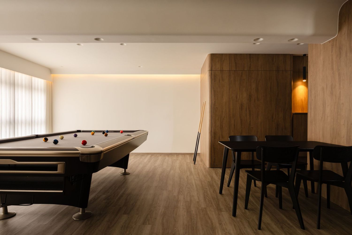 Modern game room interior with pool table and dark dining furniture on hardwood floors, illuminated by recessed lighting.