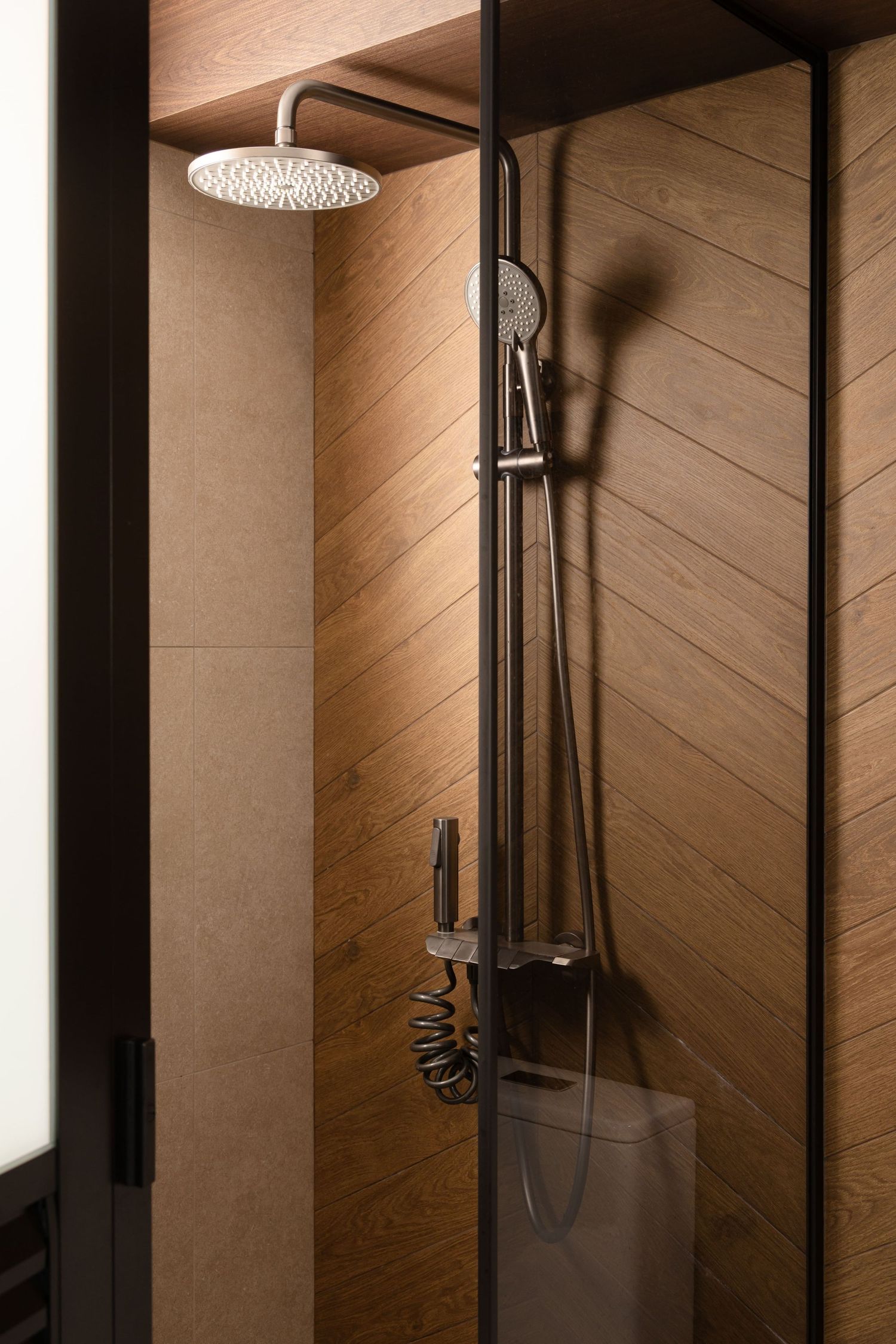 Modern bathroom interior with diagonal wood paneling and sleek chrome rainfall shower head against warm lighting.