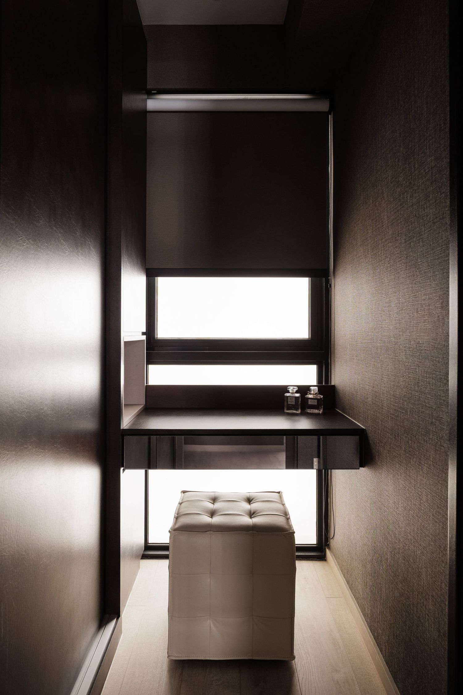 Minimalist hotel room interior with dark walls and bright window light creating dramatic contrast and shadows.