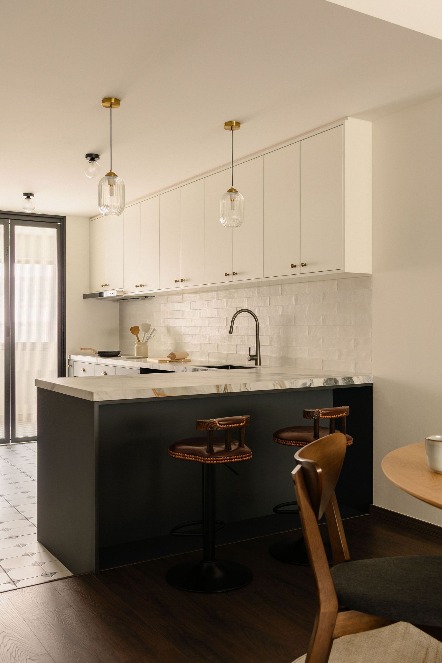 Modern kitchen with dark lower cabinets, white upper cabinets, subway tile backsplash, marble countertop, and brass pendant lights.