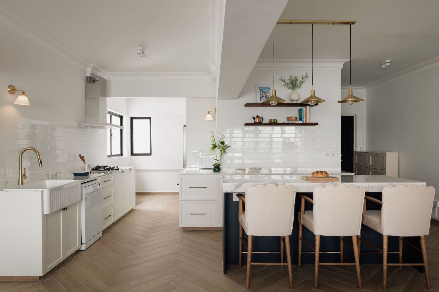 Modern white kitchen with herringbone floors, island seating, subway tile backsplash, and gold pendant lights.