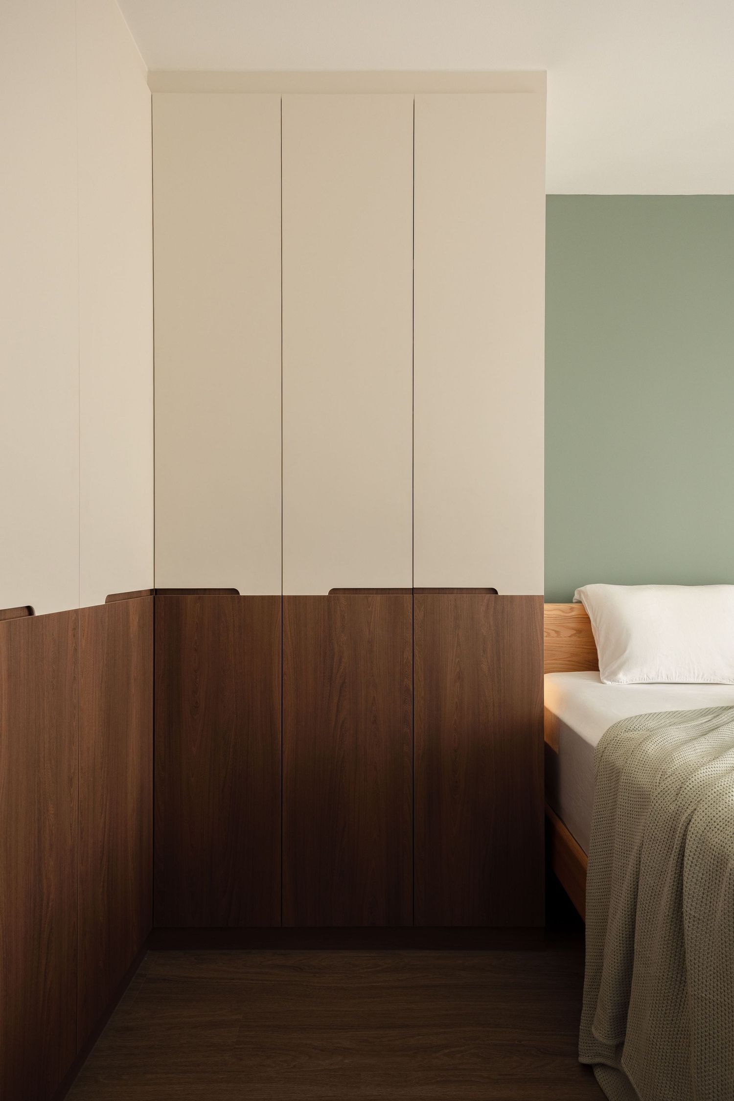 Modern bedroom with floor-to-ceiling white wardrobe, walnut wood paneling, and sage green accent wall beside a neatly made bed.