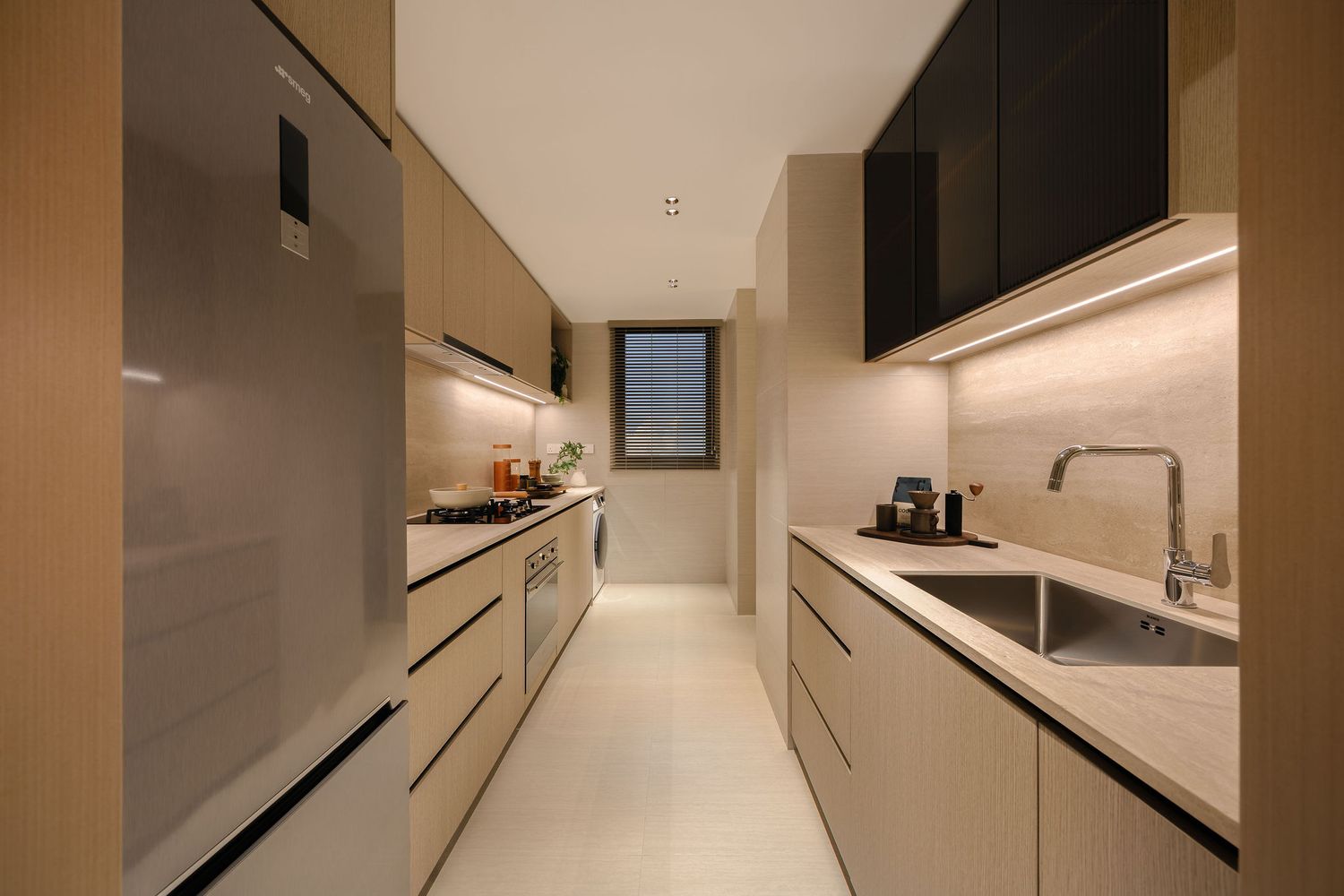 Modern galley kitchen with light wood cabinetry, stainless steel sink and faucet, built-in oven, and a window at the far end.