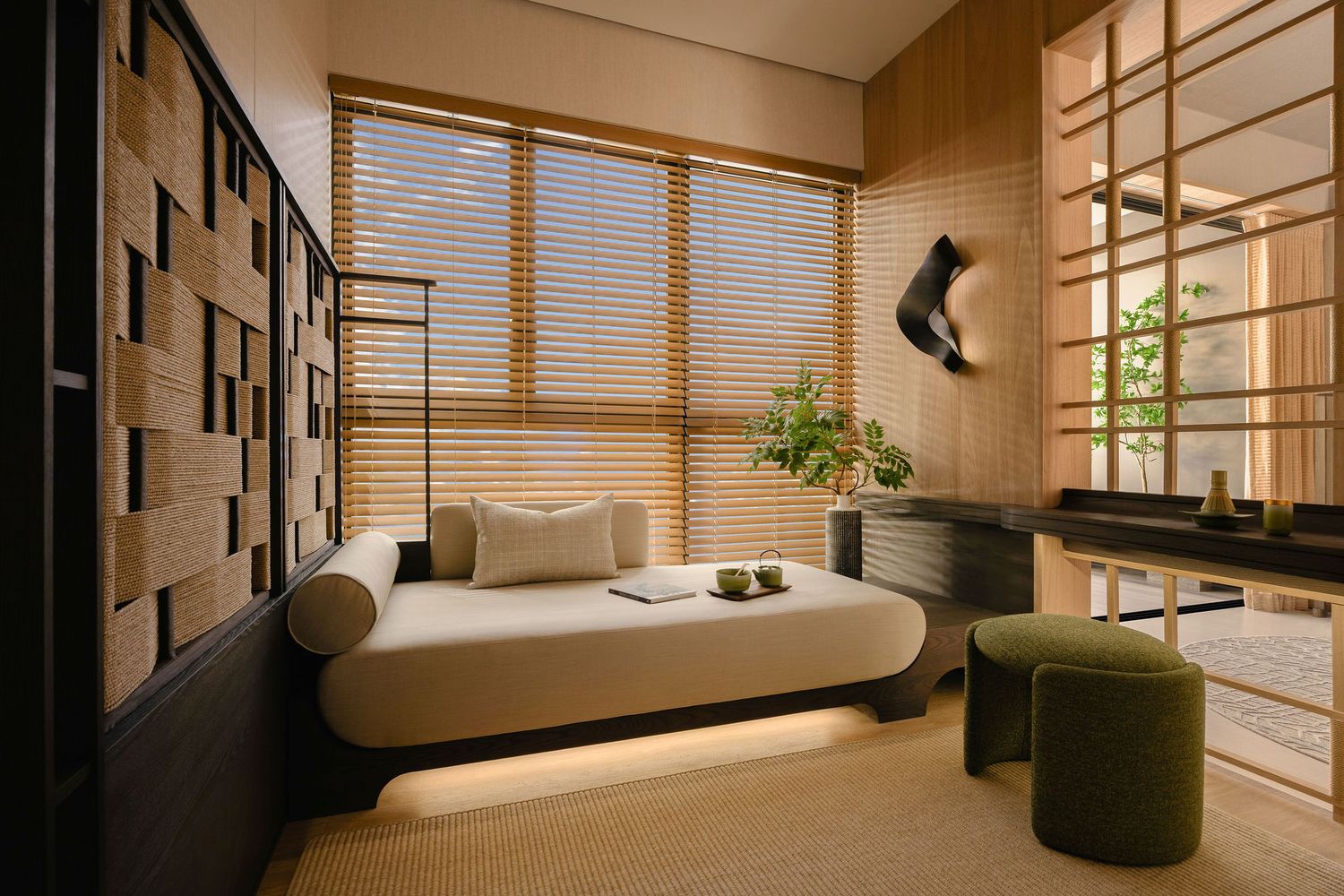Serene Japanese-inspired room with a cream daybed, wooden blinds, green ottoman, potted plant and warm slatted wood paneling.