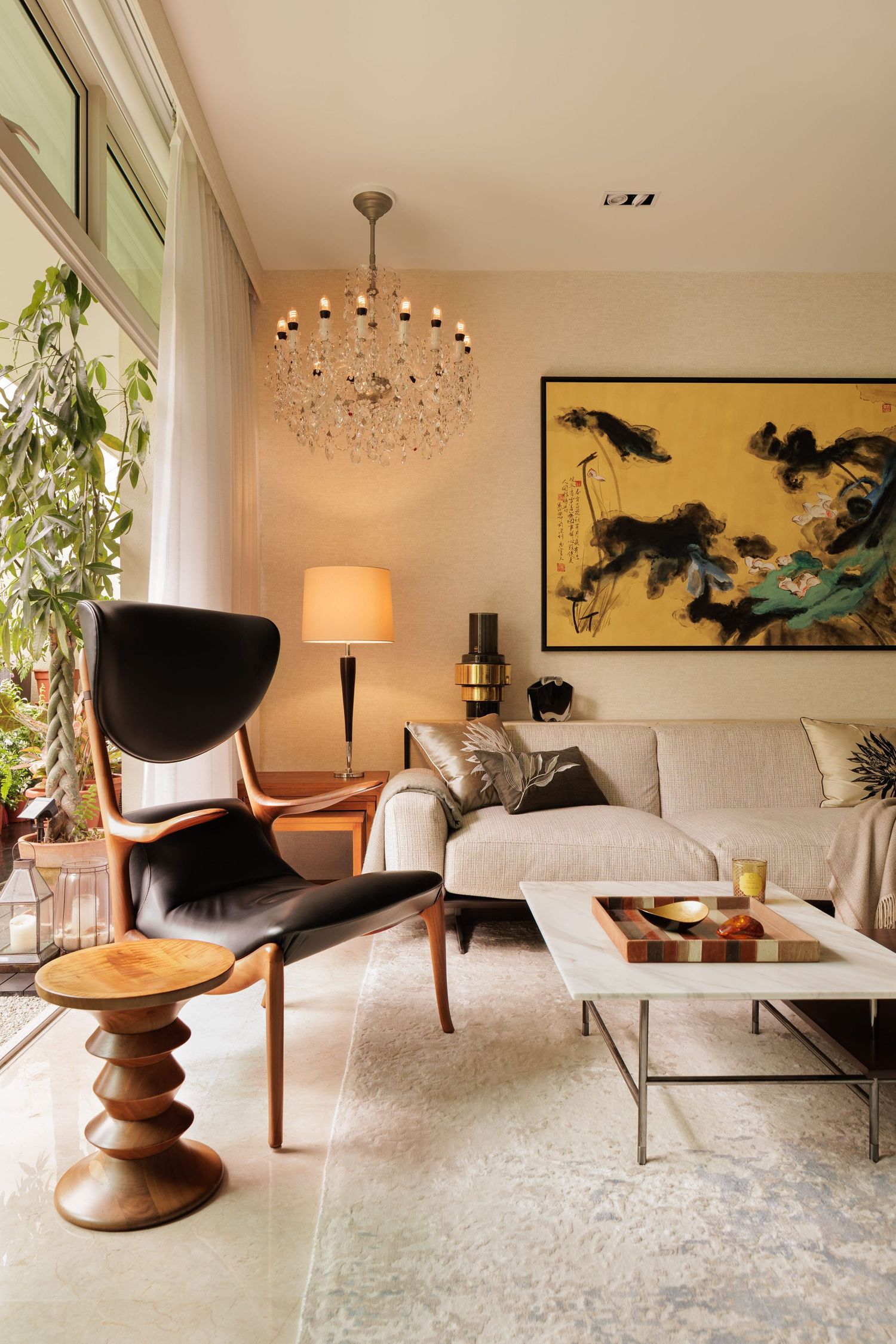 Modern living room features mid-century stool, sculptural lighting, and artwork against warm neutral decor and potted plants.