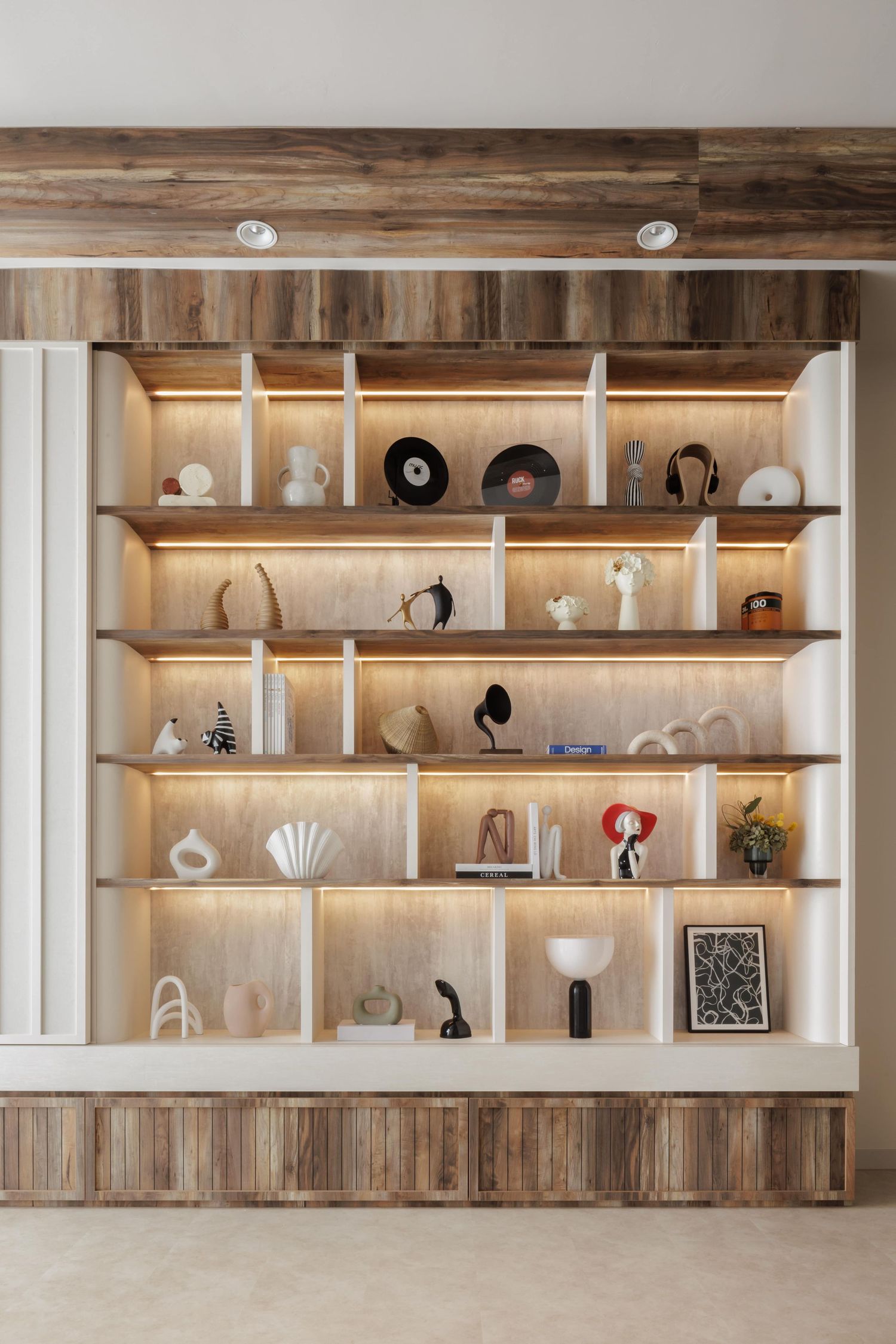Modern built-in shelving unit with backlit compartments displaying art objects, vases, and decorative items on wooden panels.