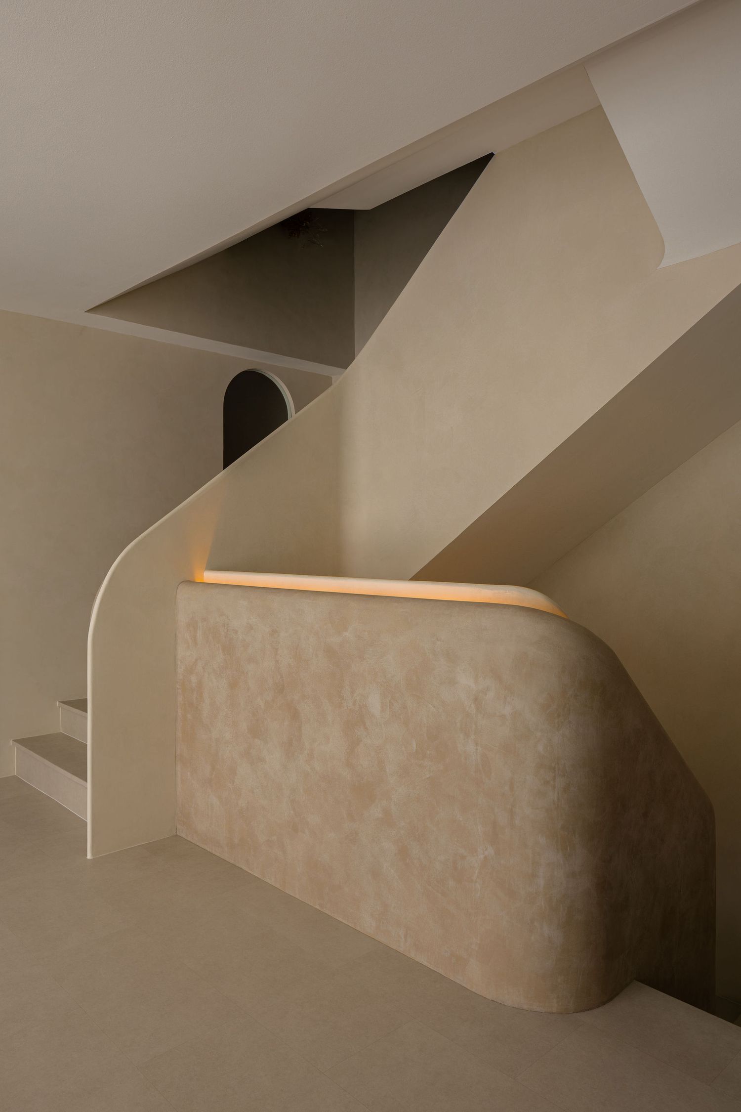 Minimalist beige staircase with curved walls, subtle LED lighting, and an arched doorway in a modern interior.
