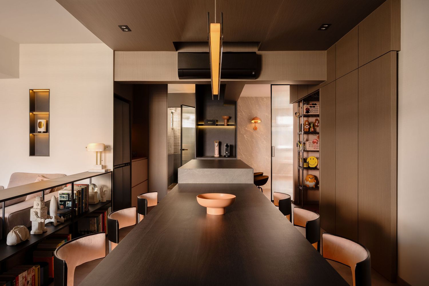 Modern open-plan dining room with dark wood table, pink chairs, pendant light, and sleek kitchen in warm neutral tones.