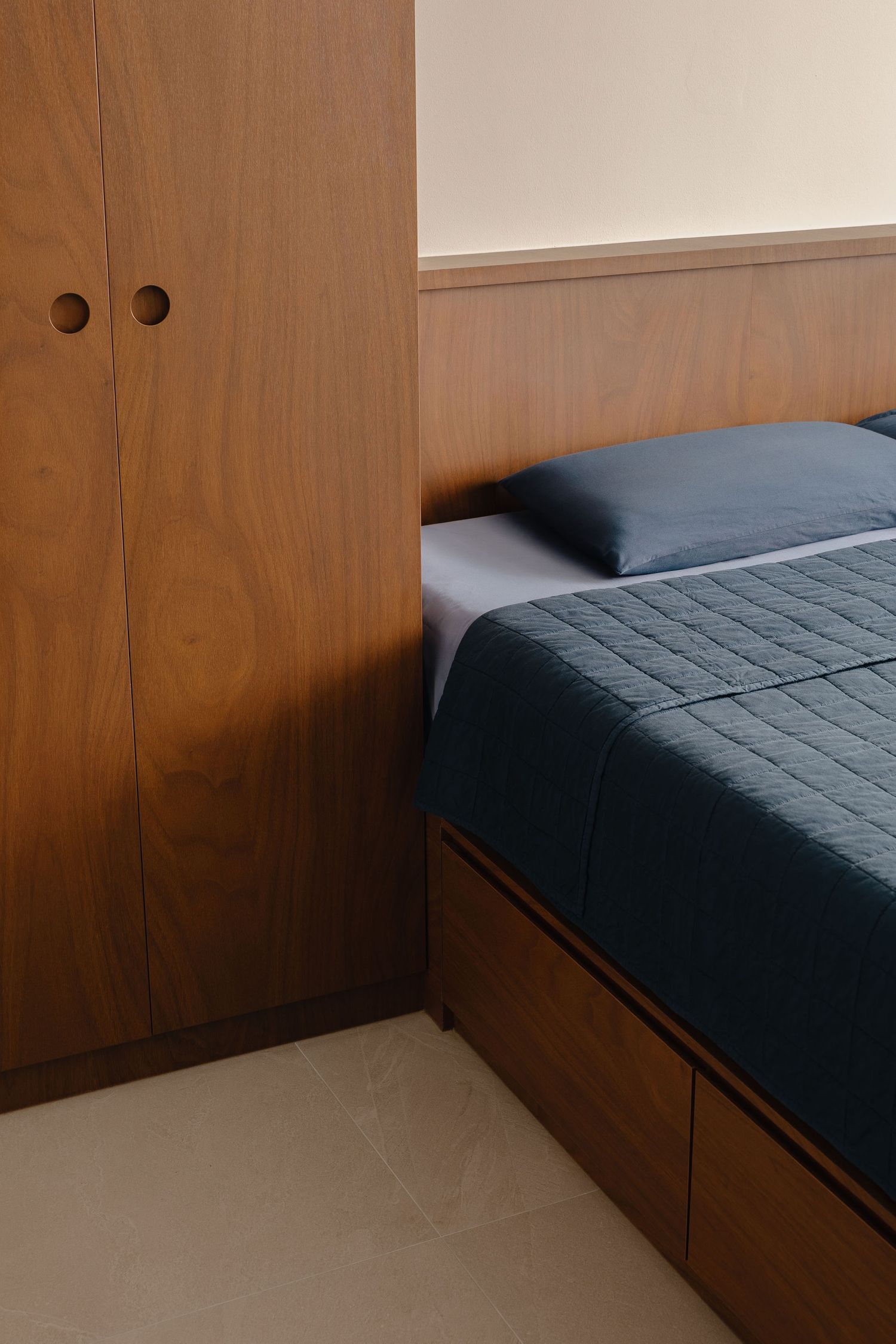 Modern bedroom with wooden wardrobe, platform bed with storage drawers, and blue quilted bedding.