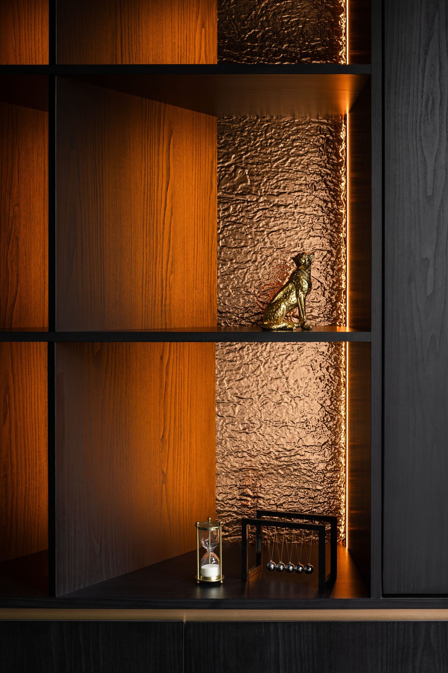 Elegant dark wood shelving unit with warm amber lighting, textured gold panel, brass figurine, and decorative glass accessories.