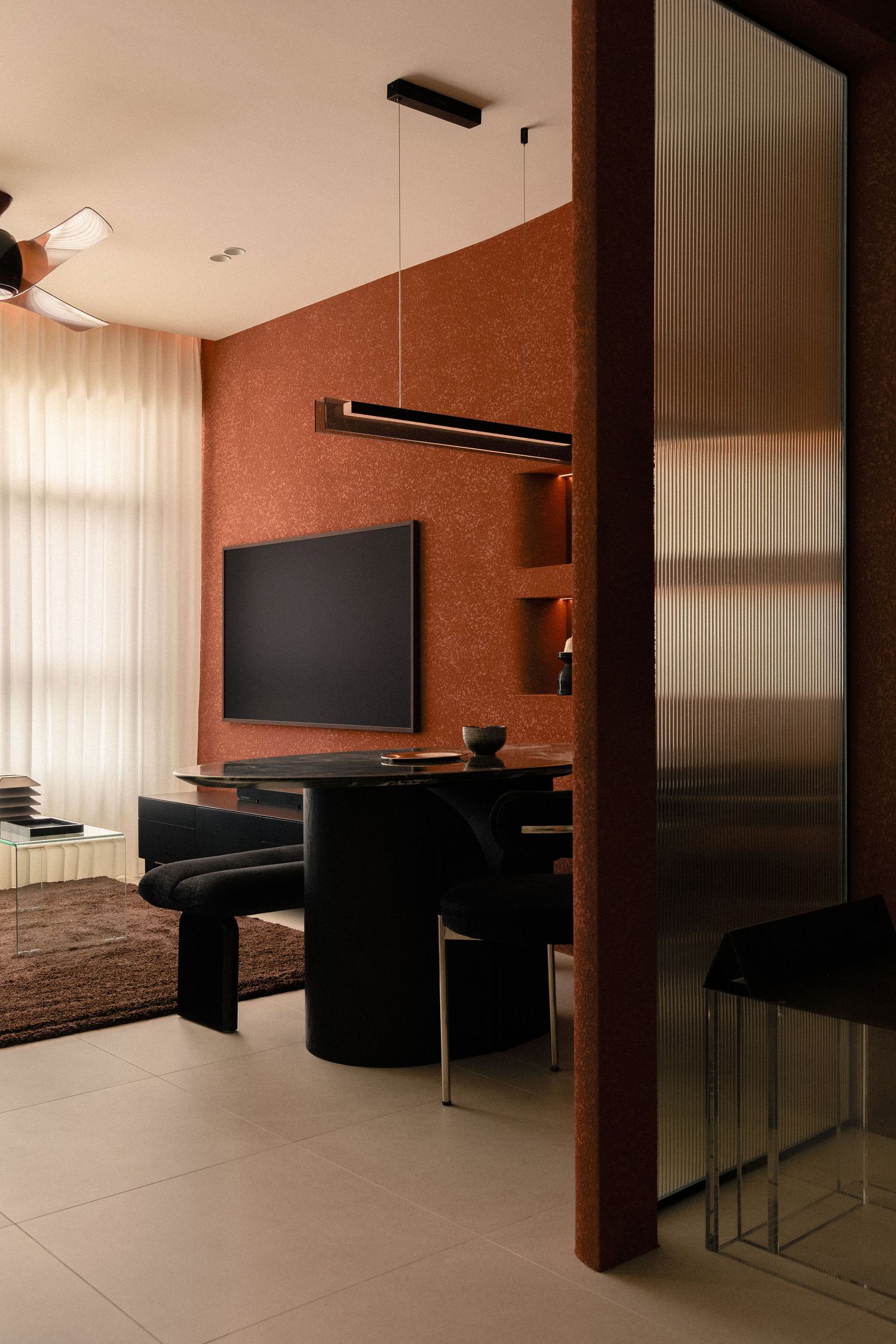 Modern living room with terracotta textured wall, wall-mounted TV, black oval dining table, linear pendant light and reeded glass partition.