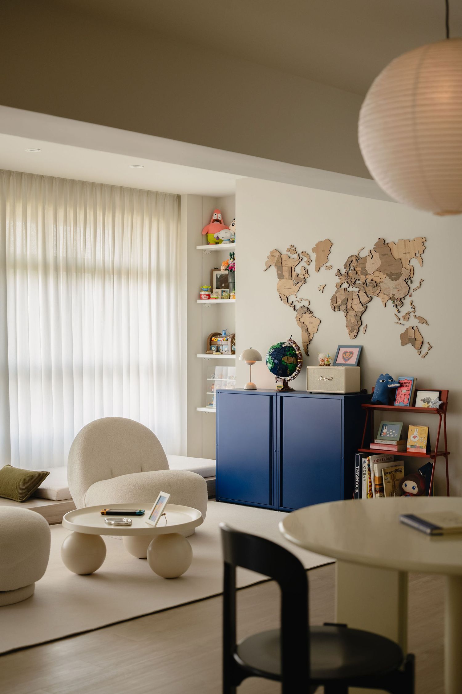 Modern living room with white lounge chair, blue cabinet, wooden world map wall art, and globe on a light wood floor.