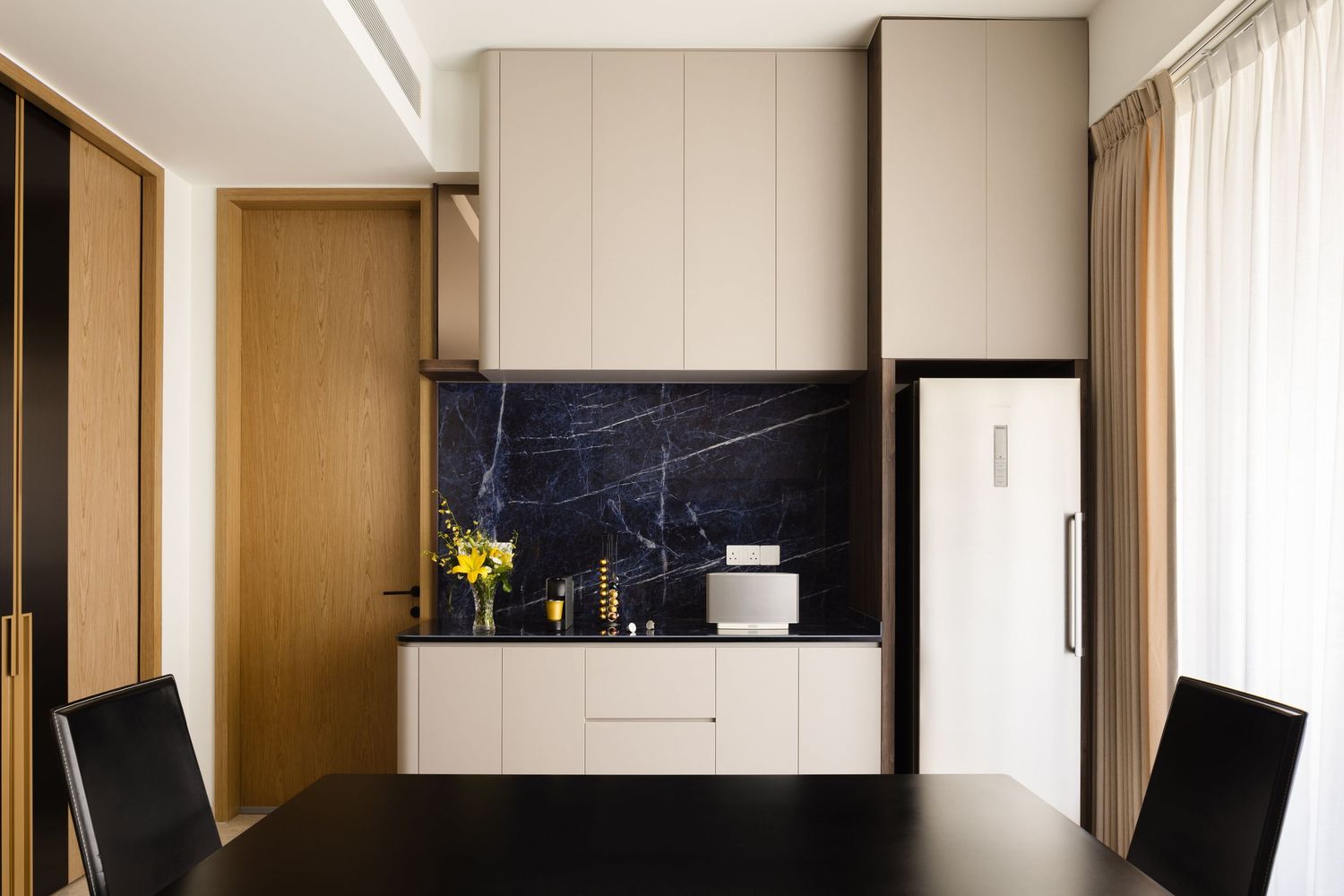 Modern kitchen with black marble backsplash, beige cabinets, white fridge and a small dining area with black chairs.