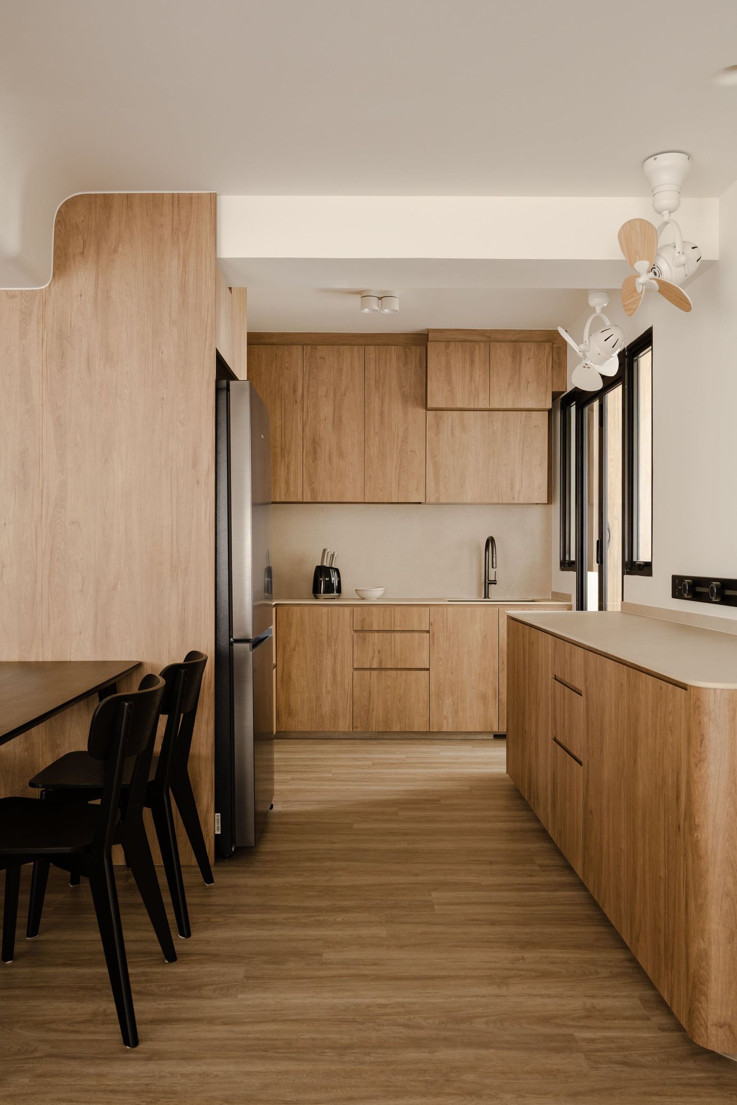 Modern minimalist kitchen with light wood cabinets, white countertops and sleek black dining chairs in a clean design.