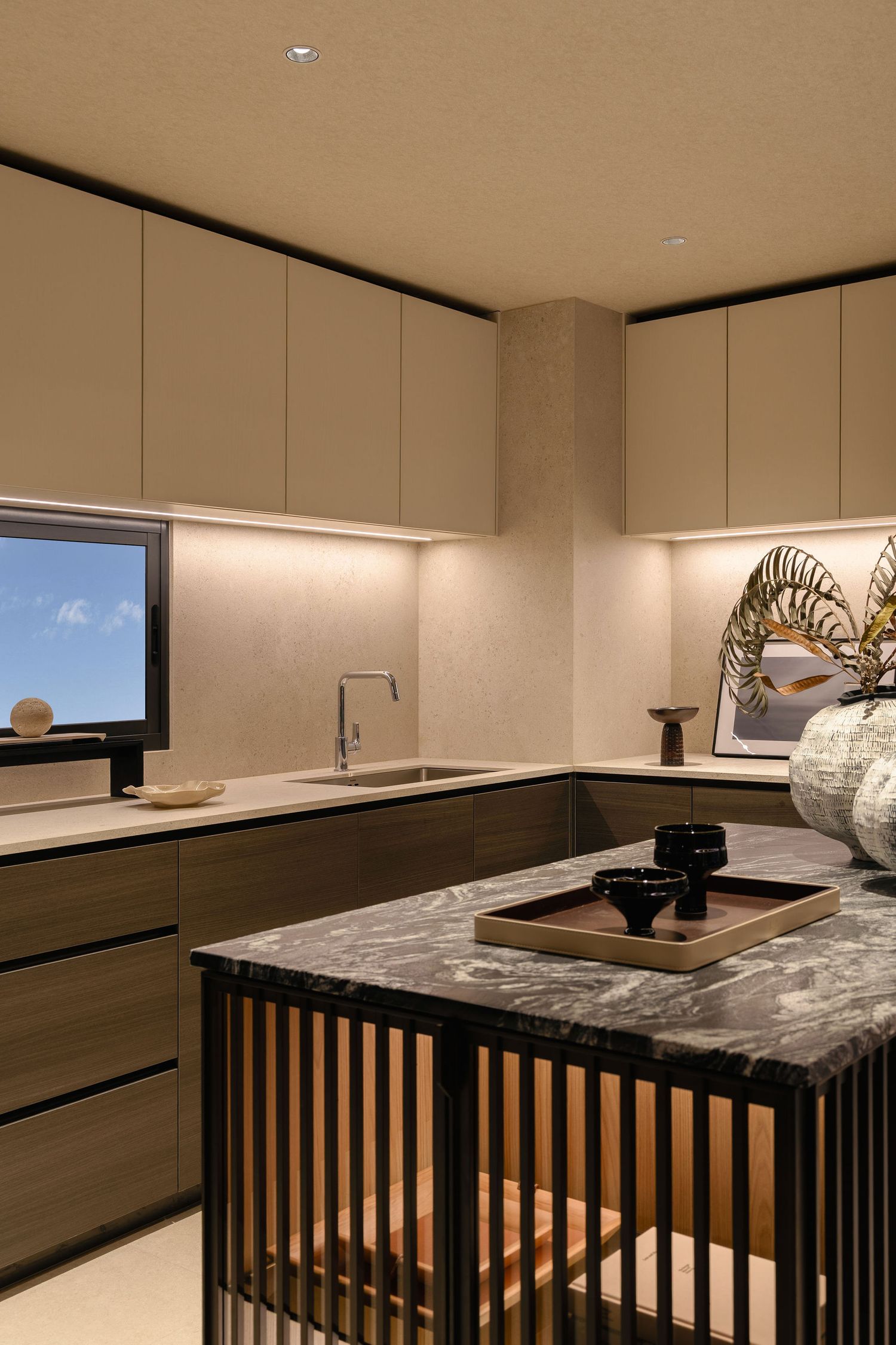 Modern kitchen with warm wood cabinets, under-cabinet lighting, a marble-top island with slatted base, and a decorative vase.