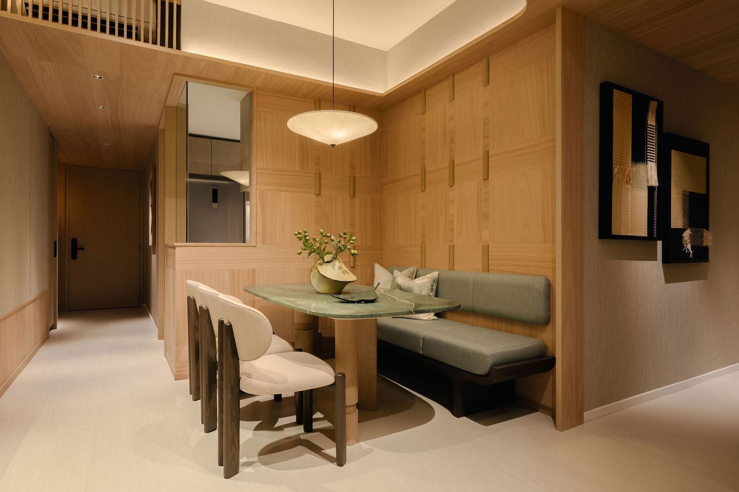 Modern dining nook with a built-in gray banquette, glass table, cream chairs and pendant light in a warm wood-paneled apartment interior.