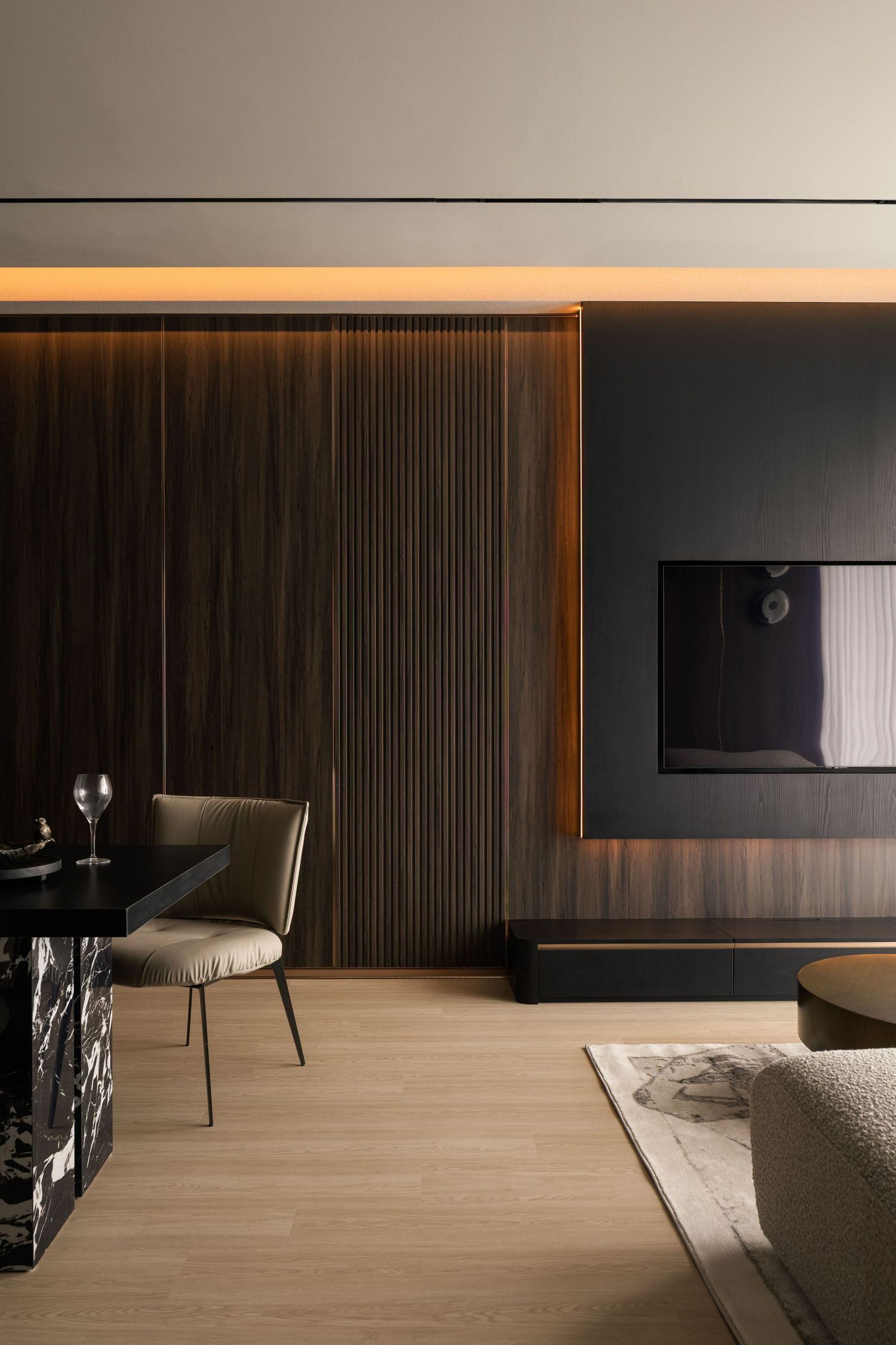 Modern luxury living room with dark wood slat wall, ambient LED lighting, marble dining table, and sleek TV unit on light hardwood floors.