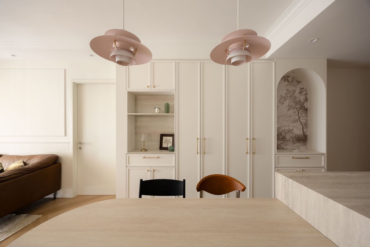Modern dining room with pink pendant lights, white built-in cabinetry, and light wood table in an elegant neutral interior.