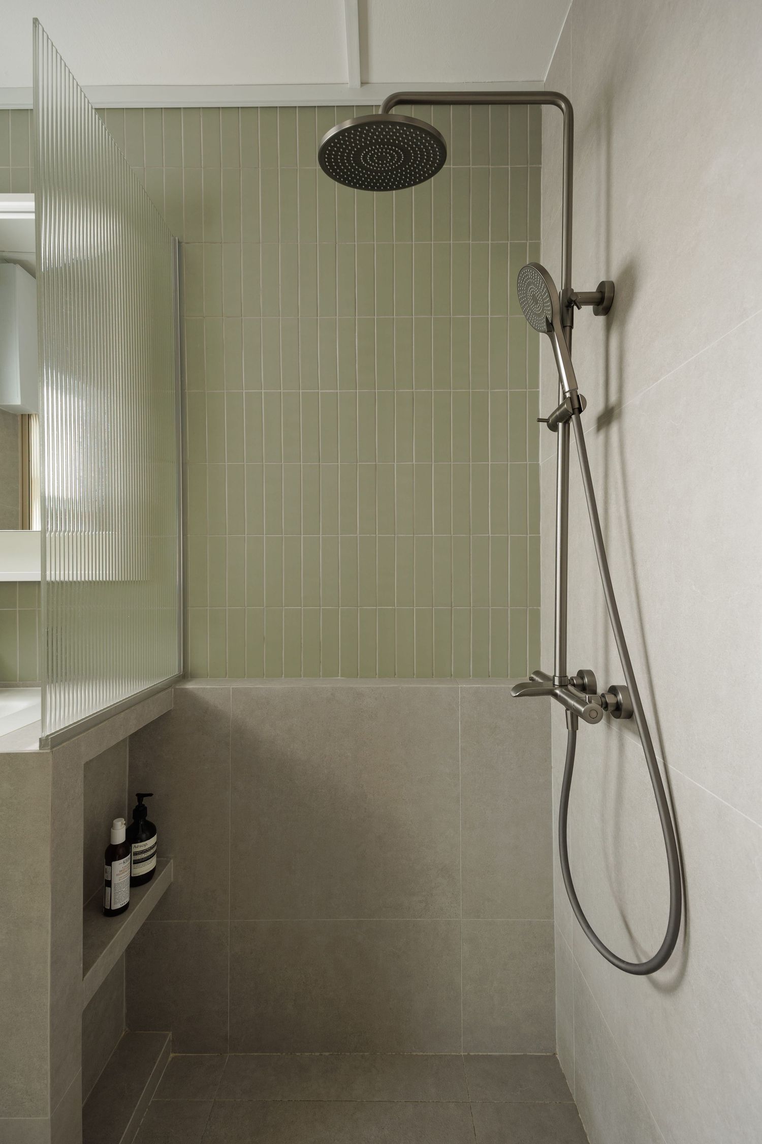 Modern walk-in shower with sage green tile walls, rainfall showerhead, and built-in shelf niche for toiletries.