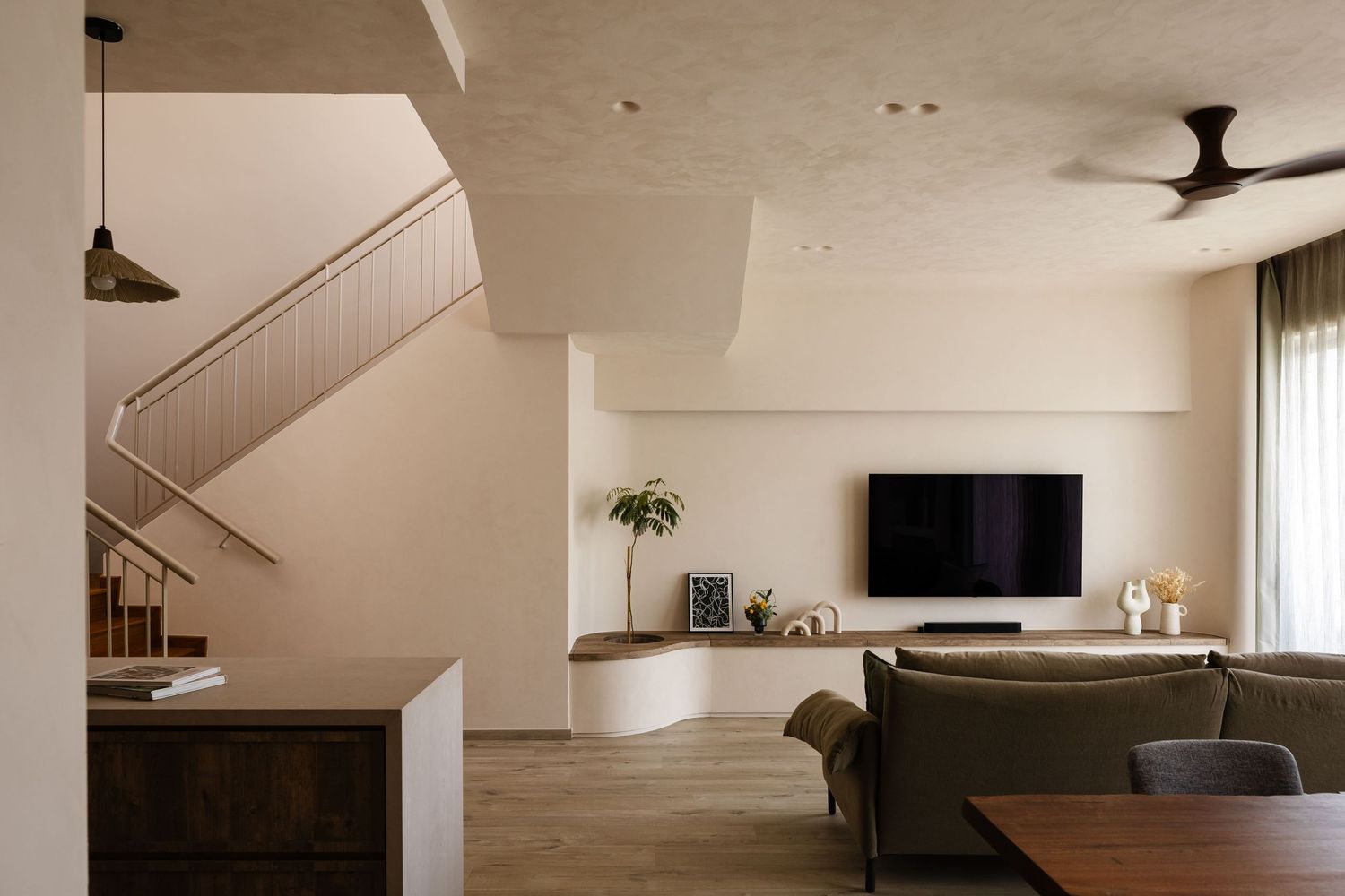 Modern minimalist living room interior with wooden floors, curved staircase, and wall-mounted TV in neutral tones.