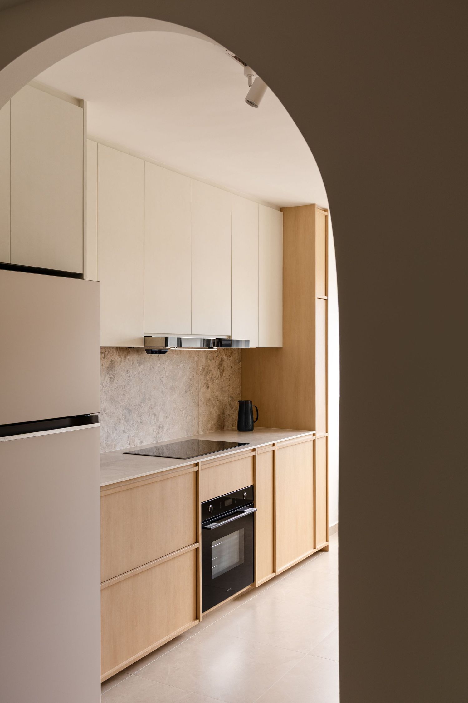 Modern minimalist kitchen with light wood cabinets and white walls featuring a curved archway entrance and built-in appliances.