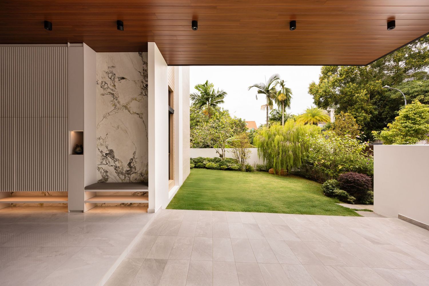 Modern stone walkway with wooden ceiling connects indoor and outdoor spaces through a sleek architectural design.