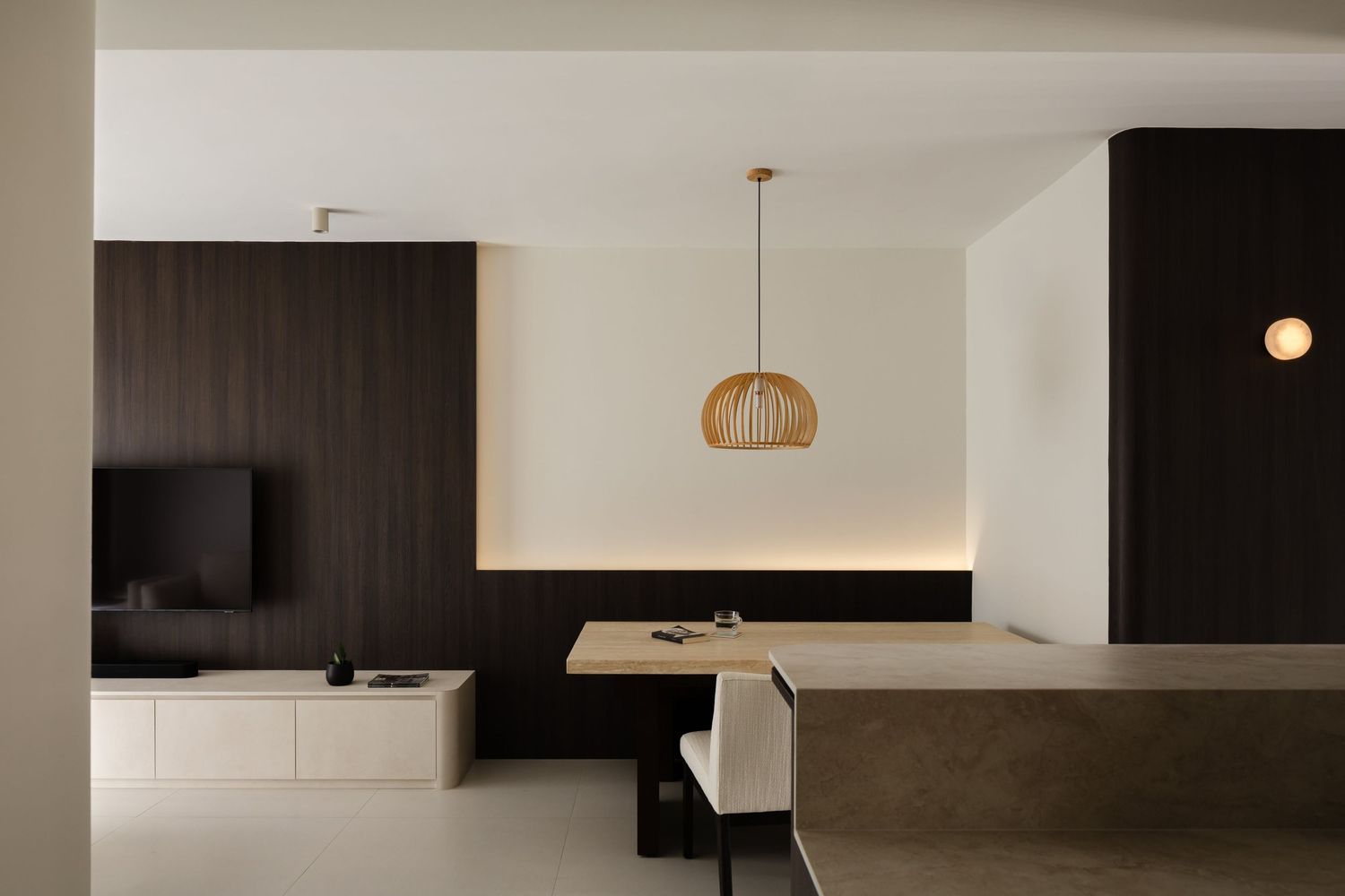 Modern minimalist interior with white walls, sleek kitchen cabinets, pendant lighting and TV mounted on dark accent wall.