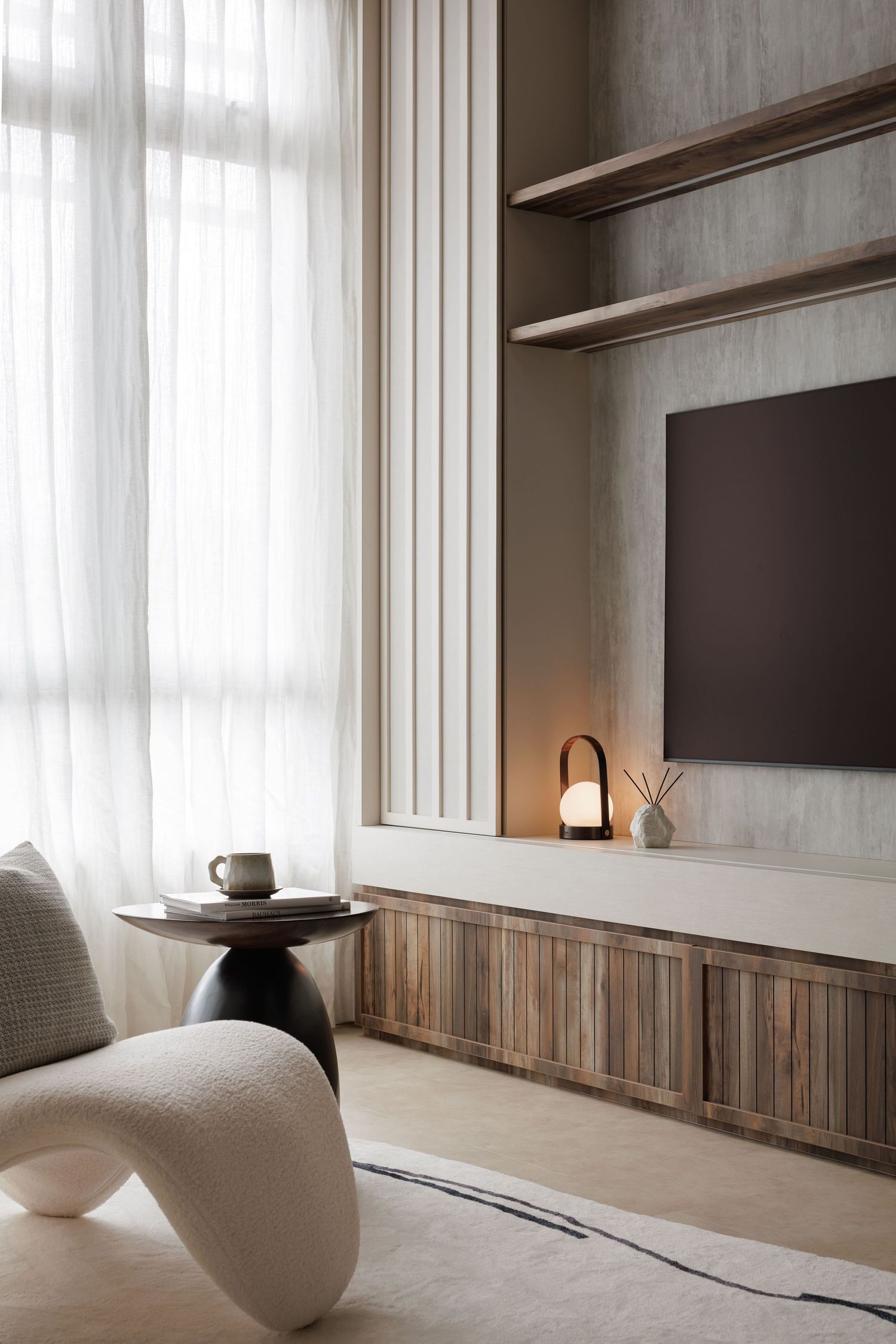 Modern living room with curved white chair, wooden media unit, sheer curtains, and minimalist decor features.