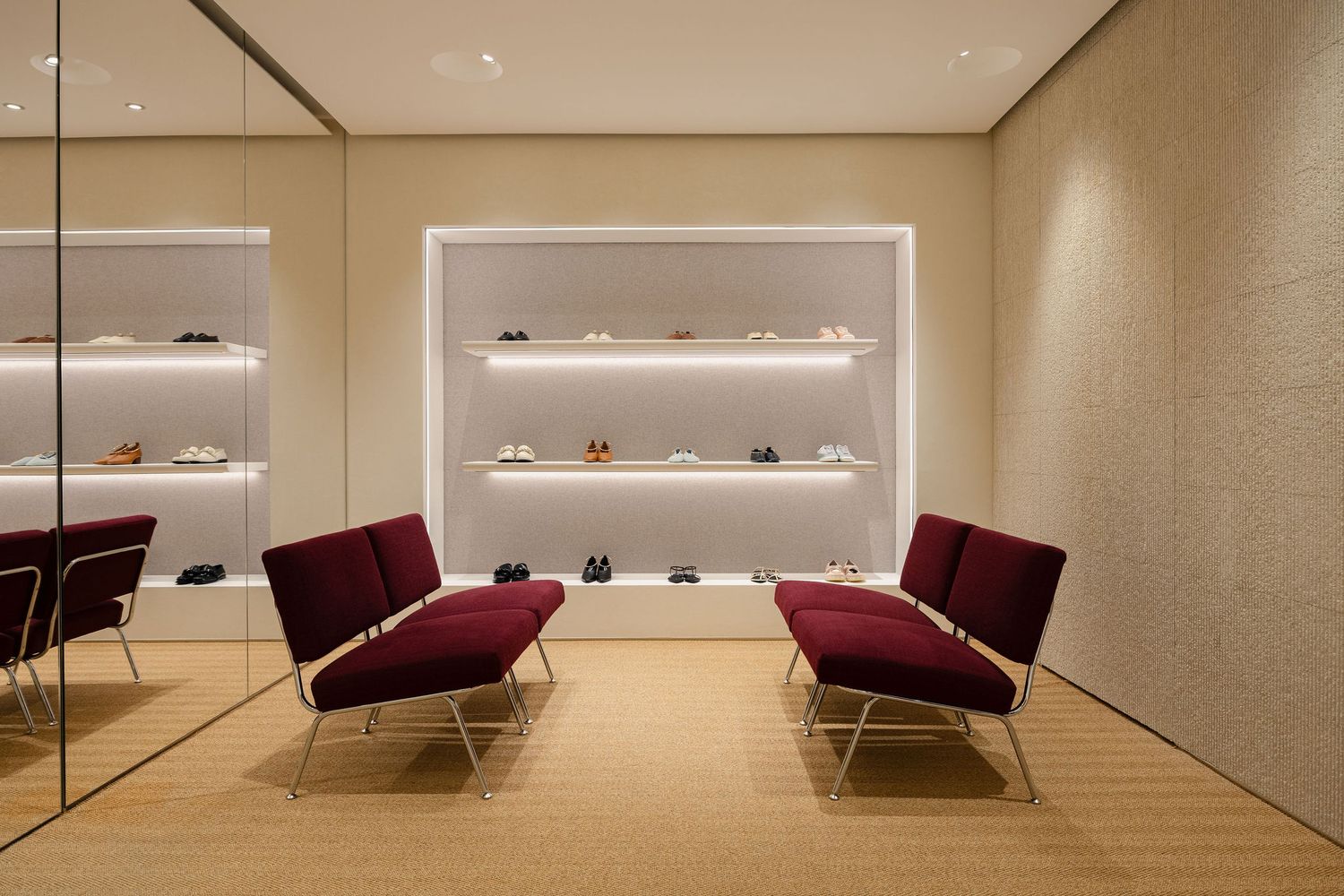 Luxury shoe store interior with burgundy chairs, illuminated shelves displaying footwear, and elegant neutral tones.