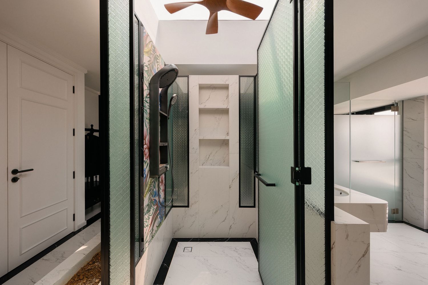 Modern bathroom with white marble floors, frosted glass doors, built-in wall niche, ceiling fan and colorful art accent wall.