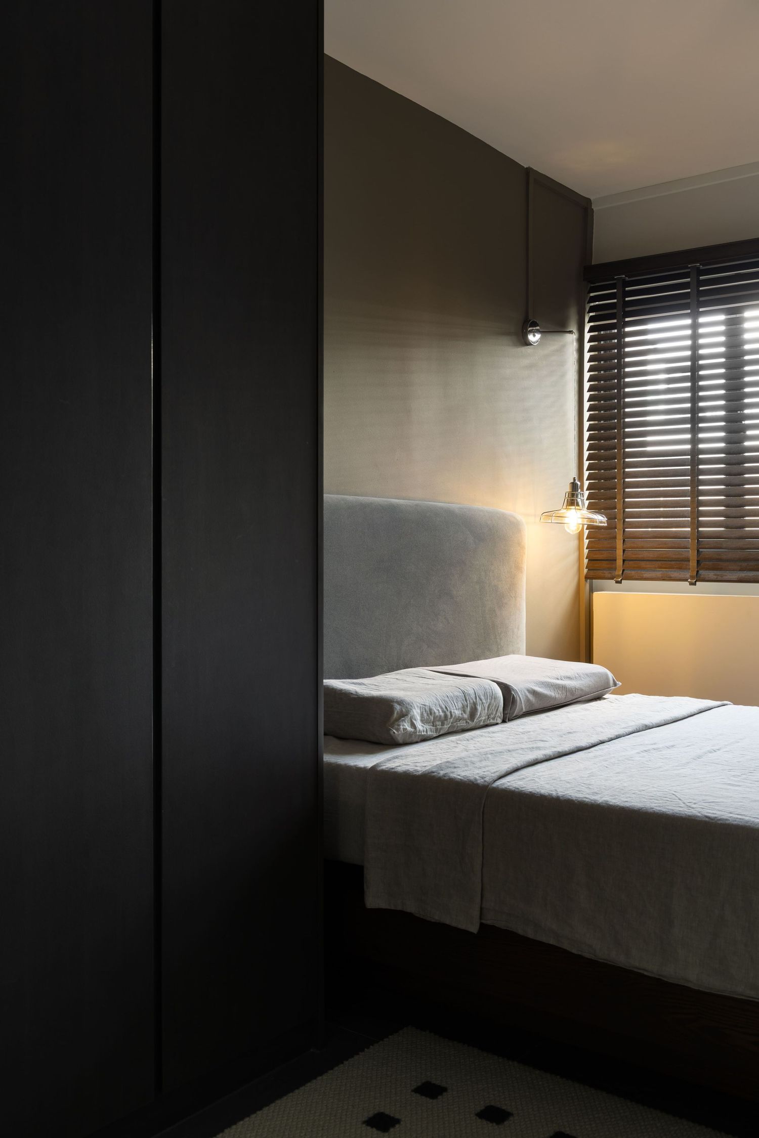 Modern minimalist bedroom with dark walls features a white bed illuminated by warm accent lighting from above.