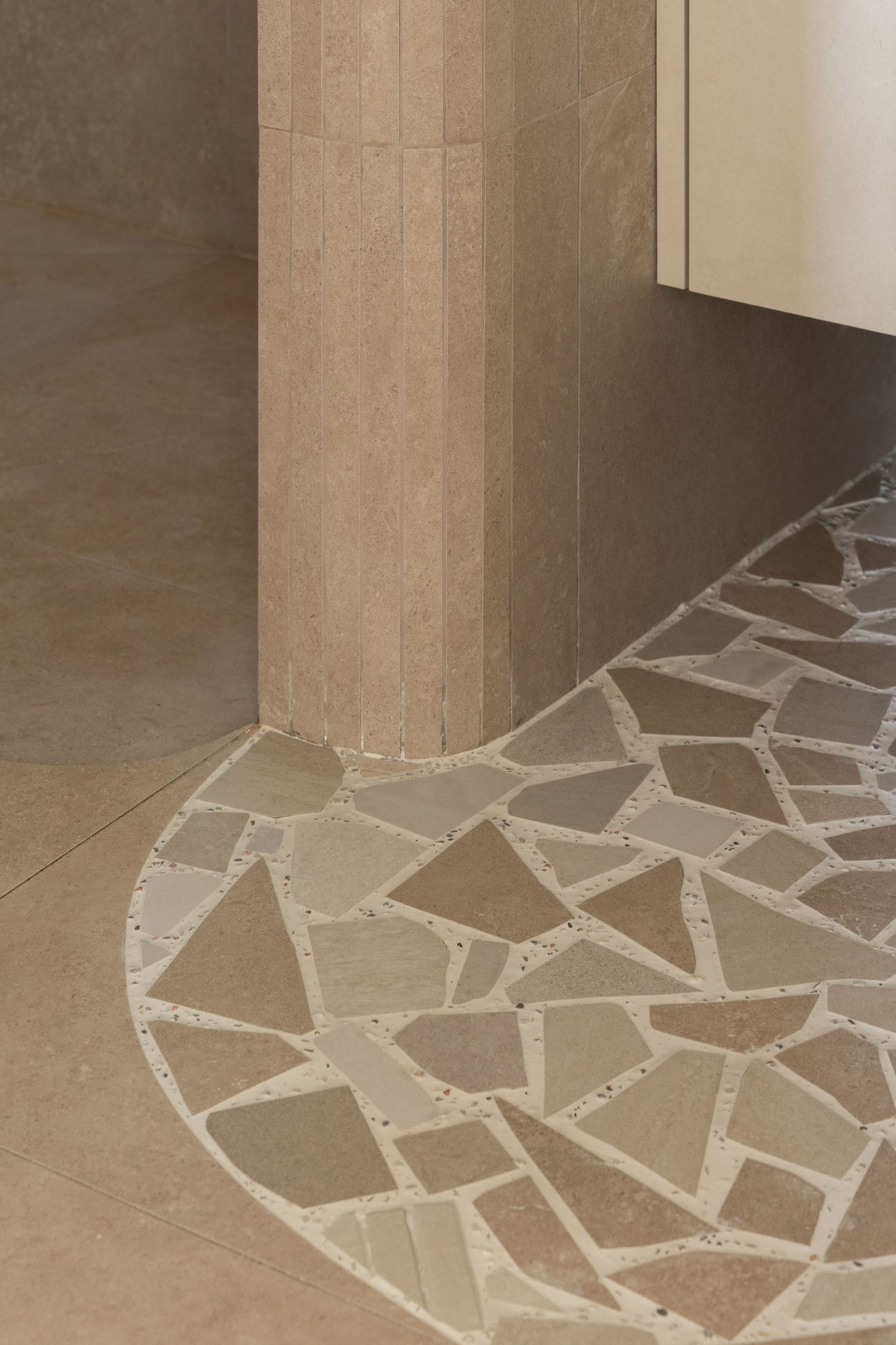 Beige stone columns with a decorative broken tile mosaic pattern on the floor create an elegant architectural detail.