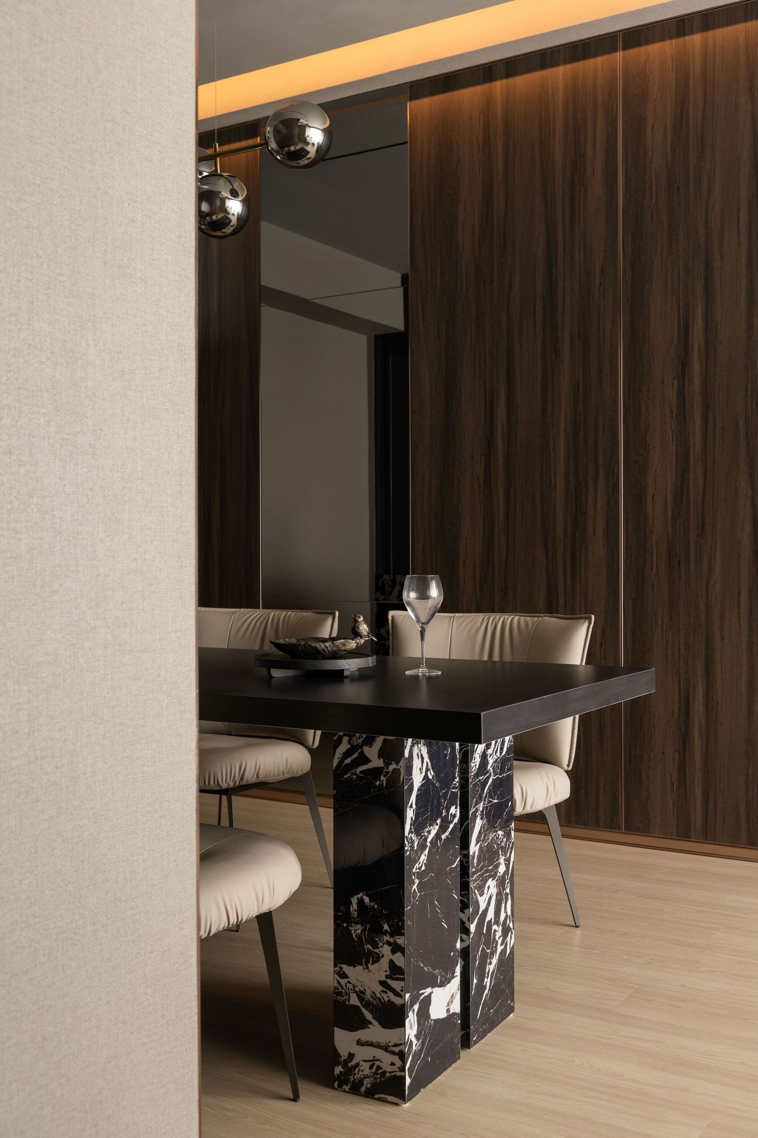 Elegant dining area with black marble table, beige chairs, globe pendant lights, and dark wood panel wall accents.