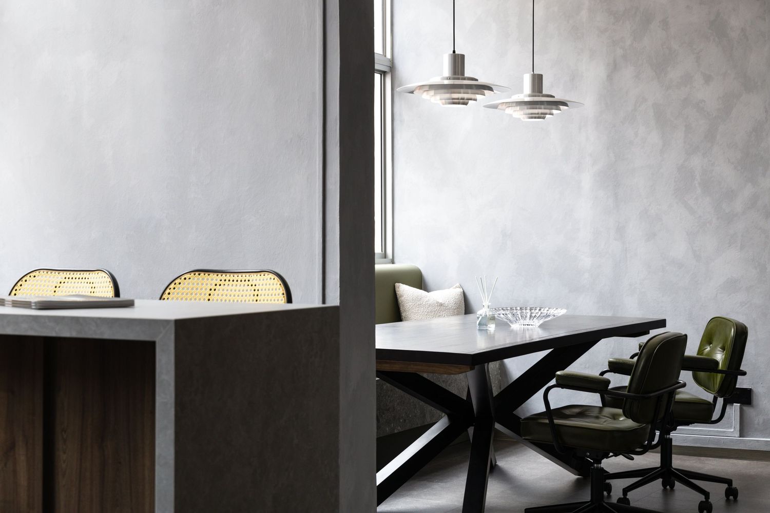 Modern minimalist dining space with dark wooden table, vintage green chairs and pendant lighting in a concrete-walled room.