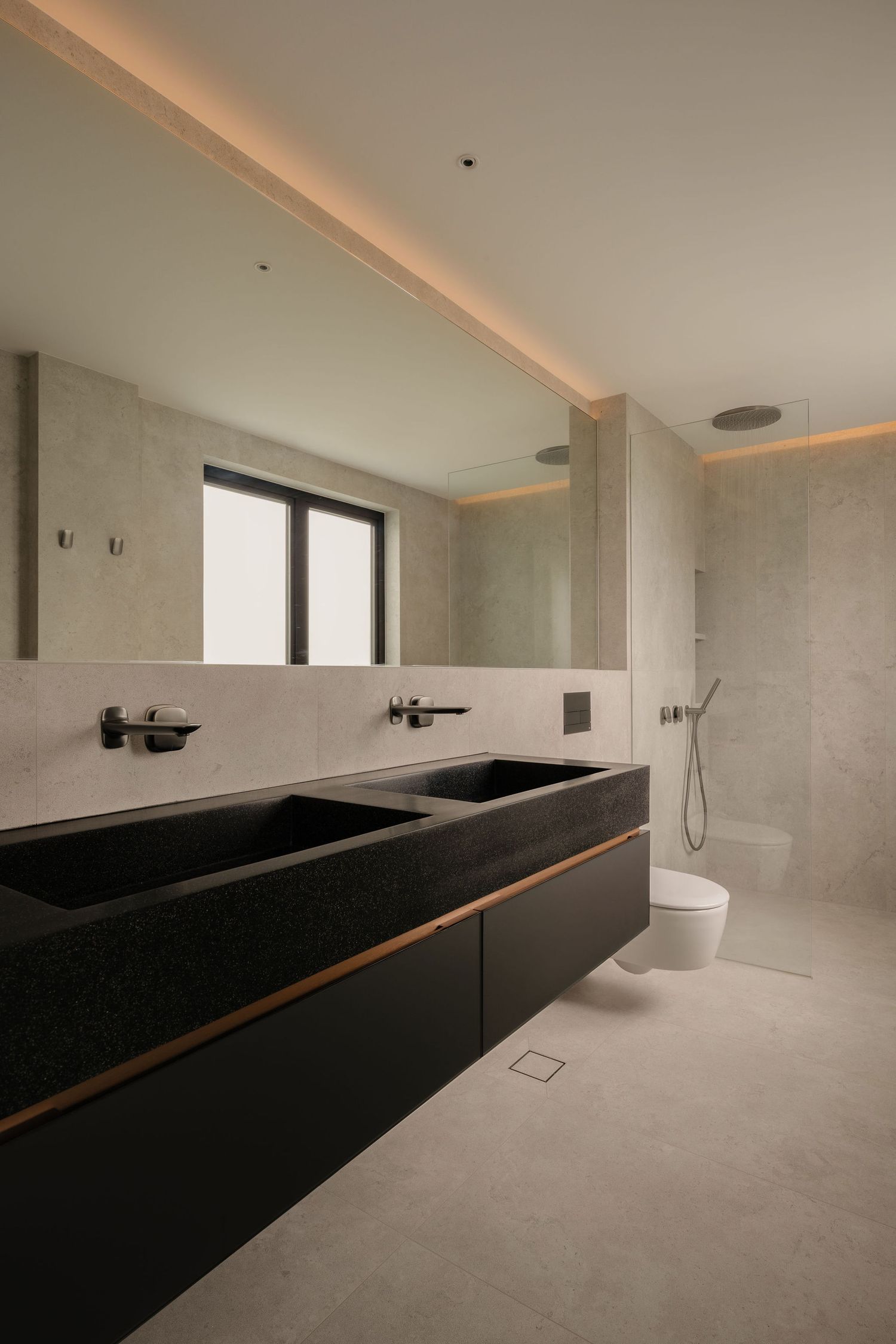 Modern minimalist bathroom with black double sink vanity, large mirror, and walk-in shower with grey stone tiles.