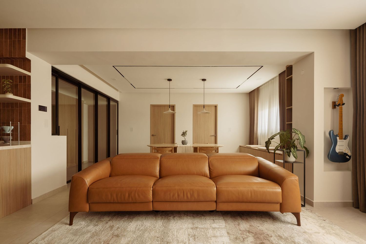 Modern living room with tan leather sofa, warm neutral tones, sliding glass doors, and a guitar displayed on the wall.