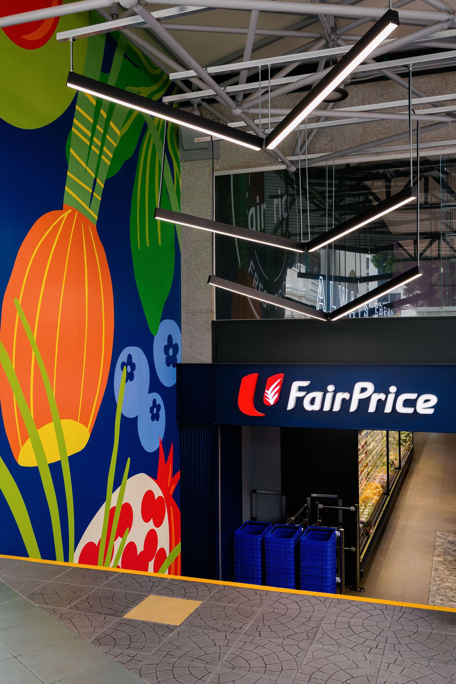 FairPrice supermarket entrance with a colorful floral and vegetable mural, modern hanging linear lights, and stacked blue shopping baskets.