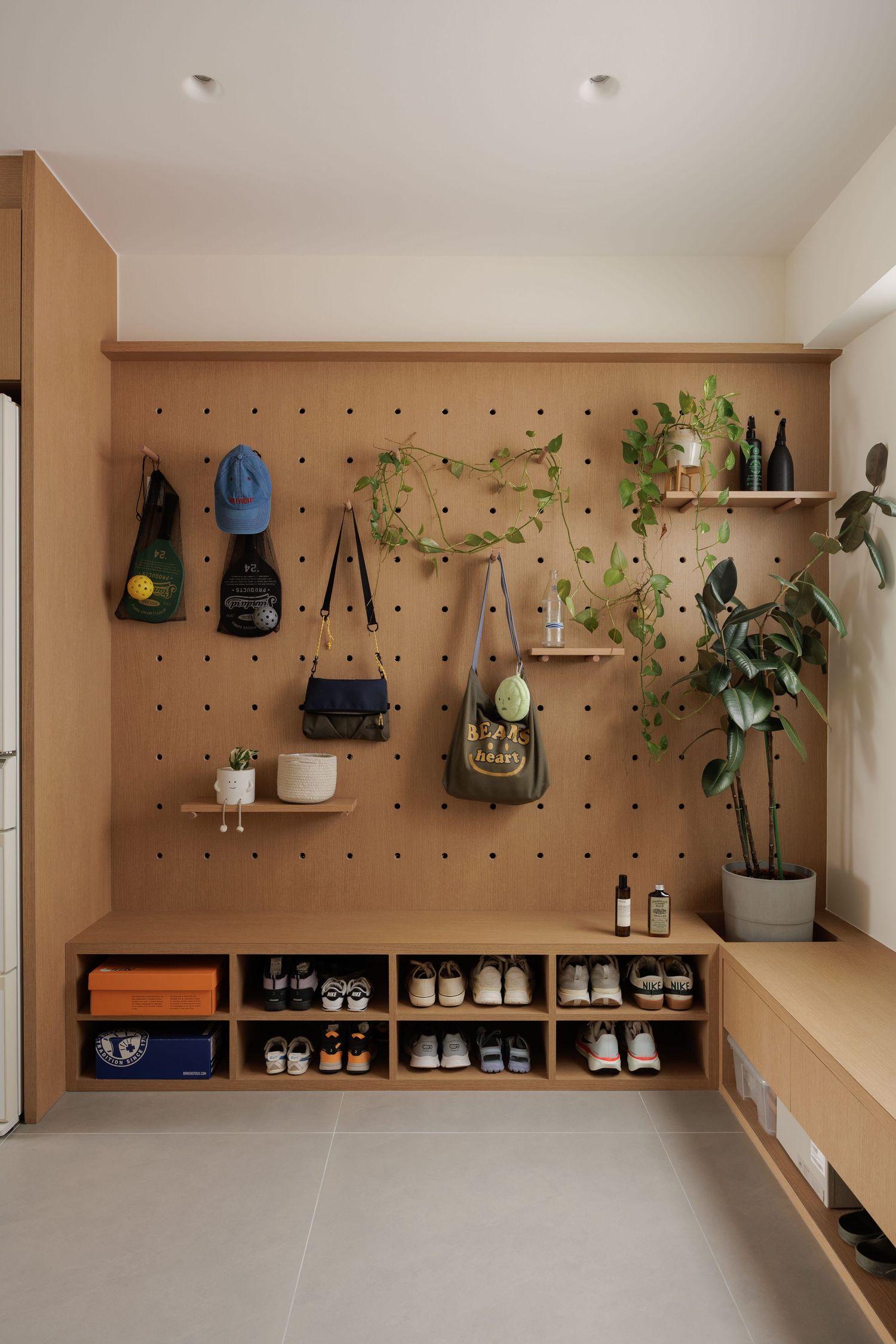 Modern pegboard wall display with hanging plants, backpacks, and shelving in a minimalist interior design setup.