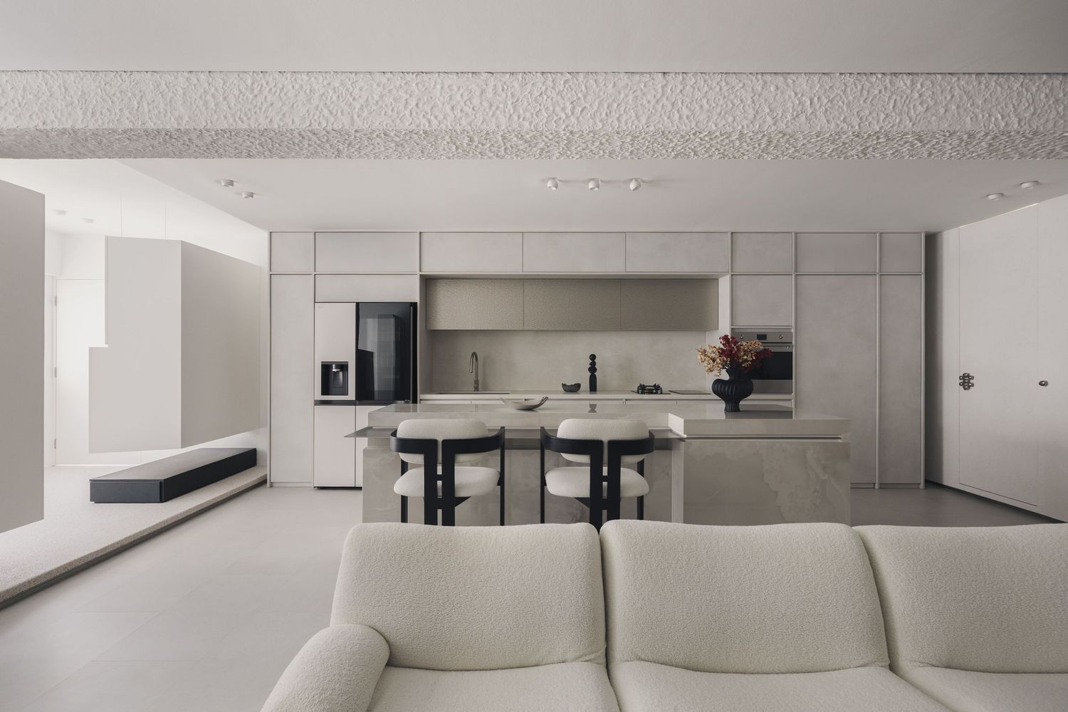Modern open-plan kitchen and living room with minimalist white design, island bar stools, and sleek cabinetry.