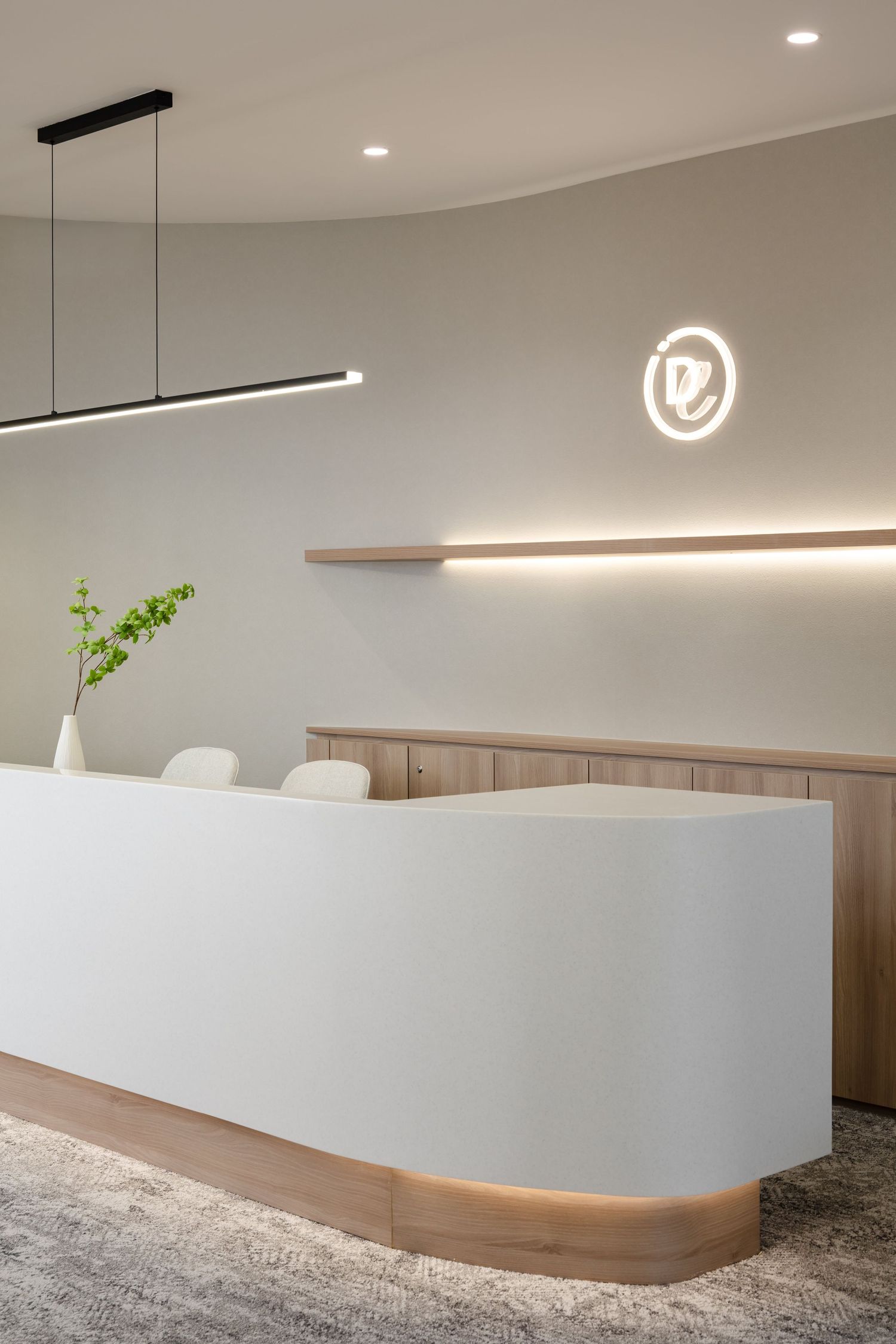 Modern minimalist reception desk with curved design features white surfaces, wood accents and illuminated logo on gray wall.