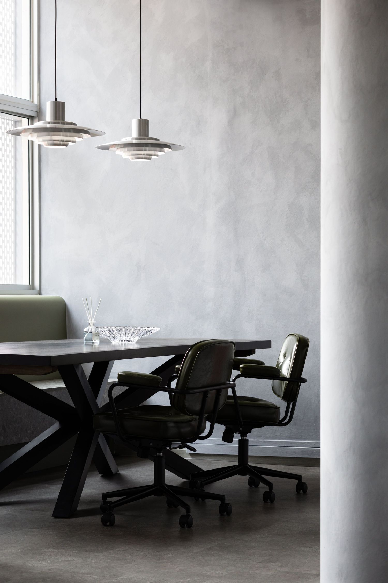 Modern office interior with black conference table, office chairs and pendant lamps against concrete wall by window.