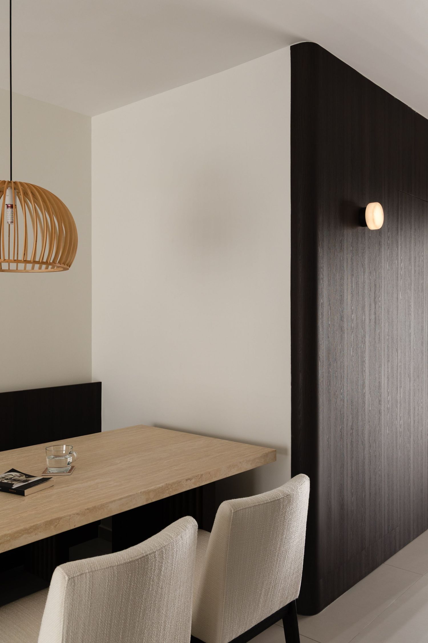 Modern minimalist workspace with wooden floating desk, white chairs and pendant light against black accent wall.
