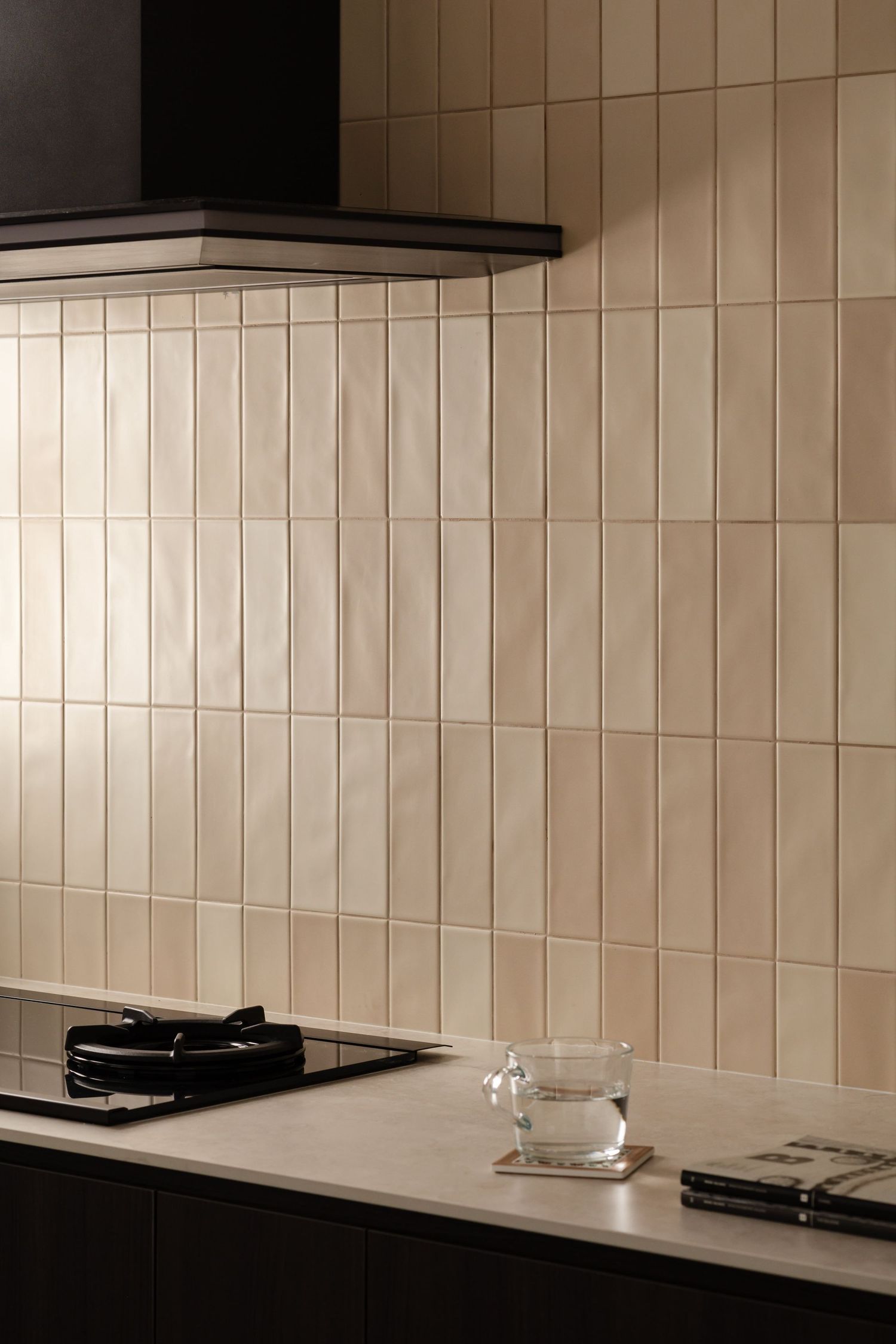 Modern kitchen interior with beige vertical subway tile backsplash, black cabinets, and white countertops.