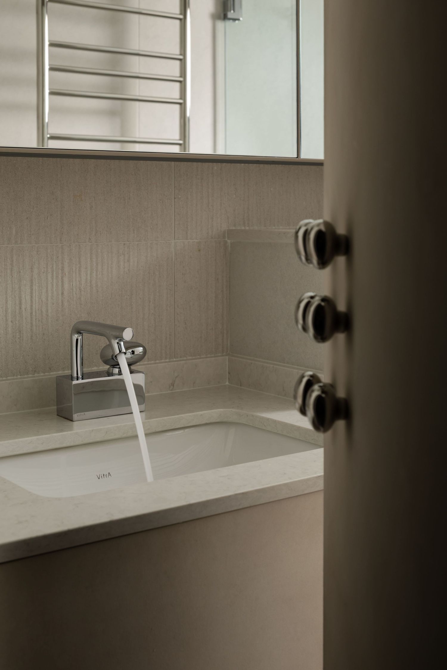 Minimalist bathroom interior with white sink basin and chrome faucet against neutral beige tiled wall.