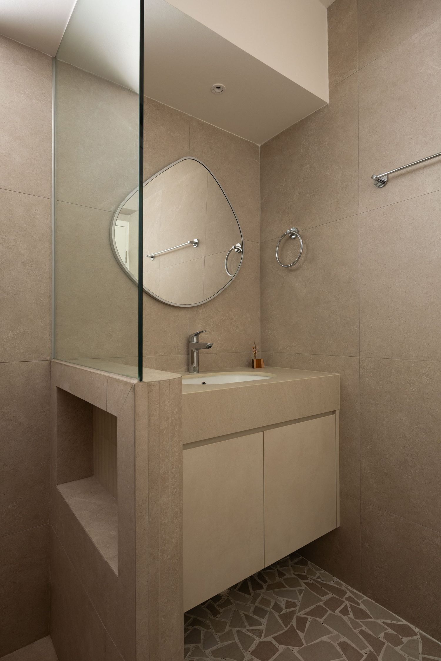 Modern minimalist bathroom with floating vanity, round mirror, and stone mosaic floor pattern in neutral beige tones.