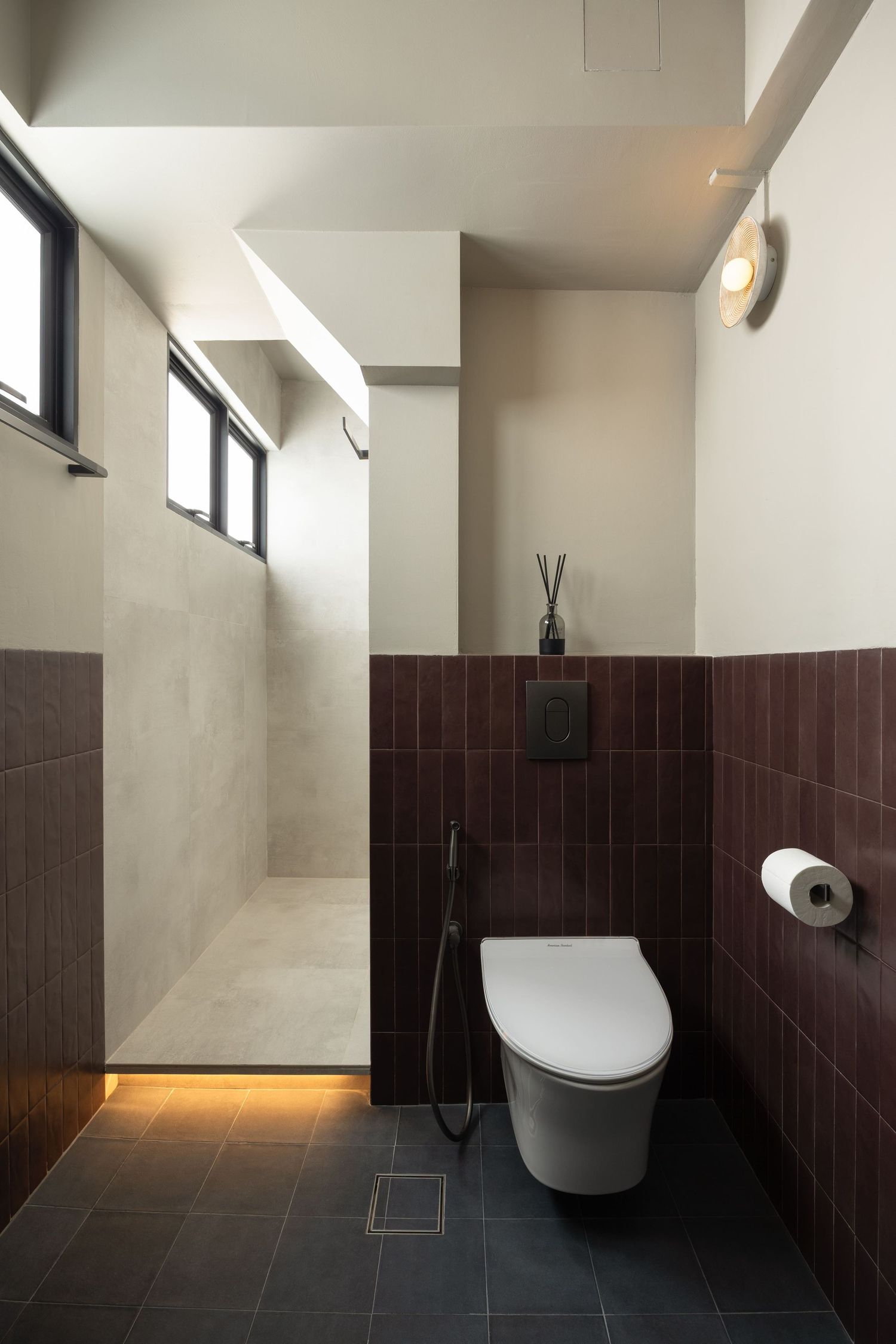 Modern bathroom interior with wall-mounted toilet, brown tile wainscoting, and minimalist design features ambient lighting.