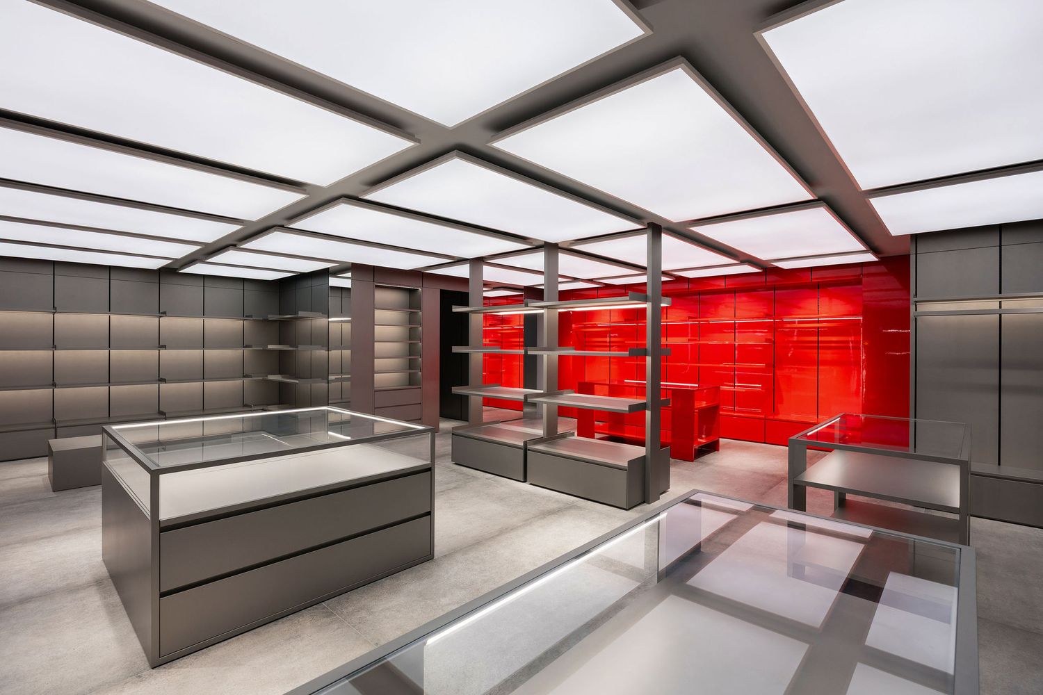 Modern retail store interior with metallic shelving, glass display cases, and vibrant red accent wall under a geometric ceiling.