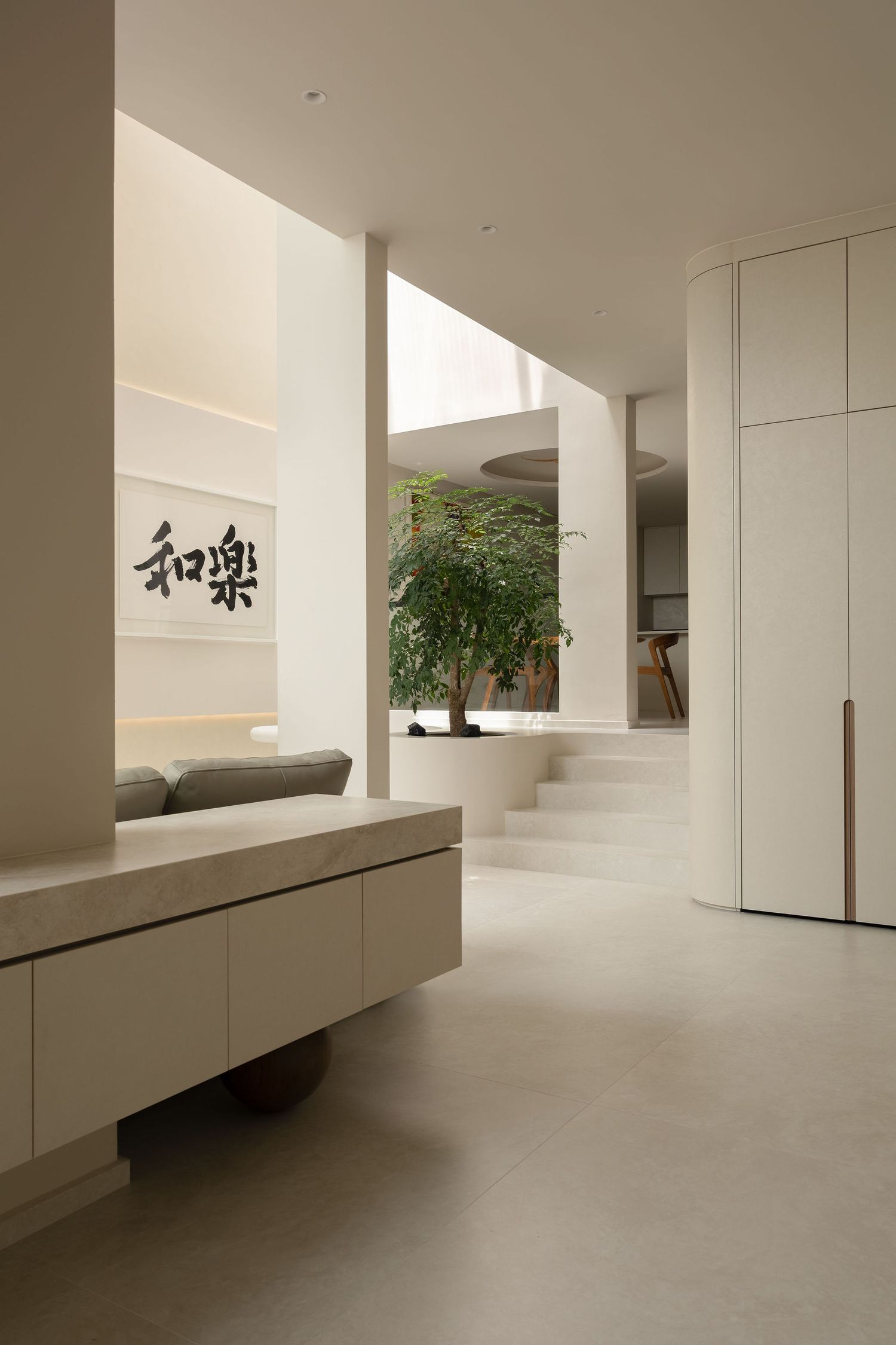 Minimalist Japanese-inspired interior with calligraphy art, floating bench, indoor tree, and neutral tones creating a serene atmosphere.